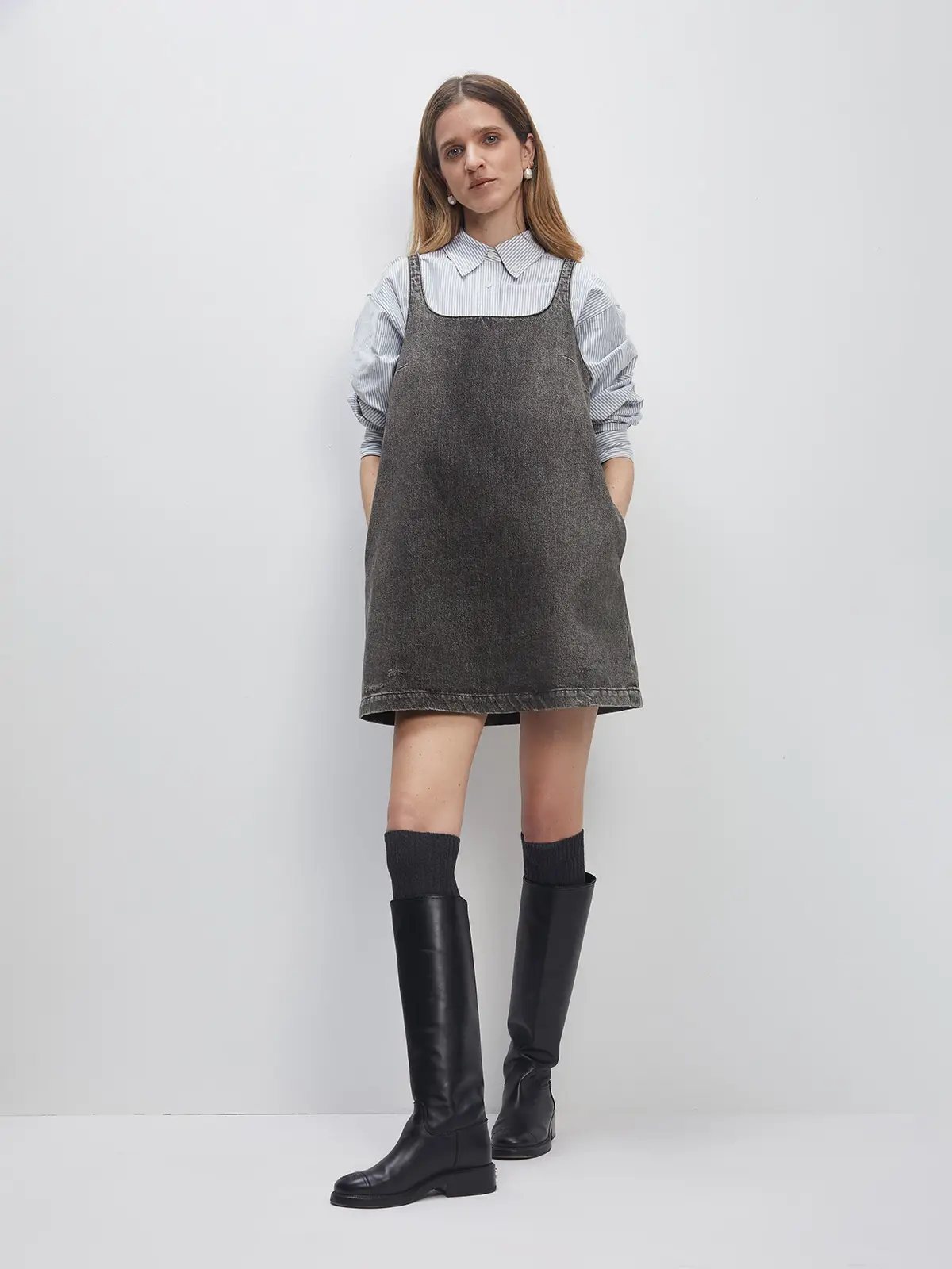 Model wearing a Dark Grey A-line denim dress over a striped collared shirt with knee-high boots.