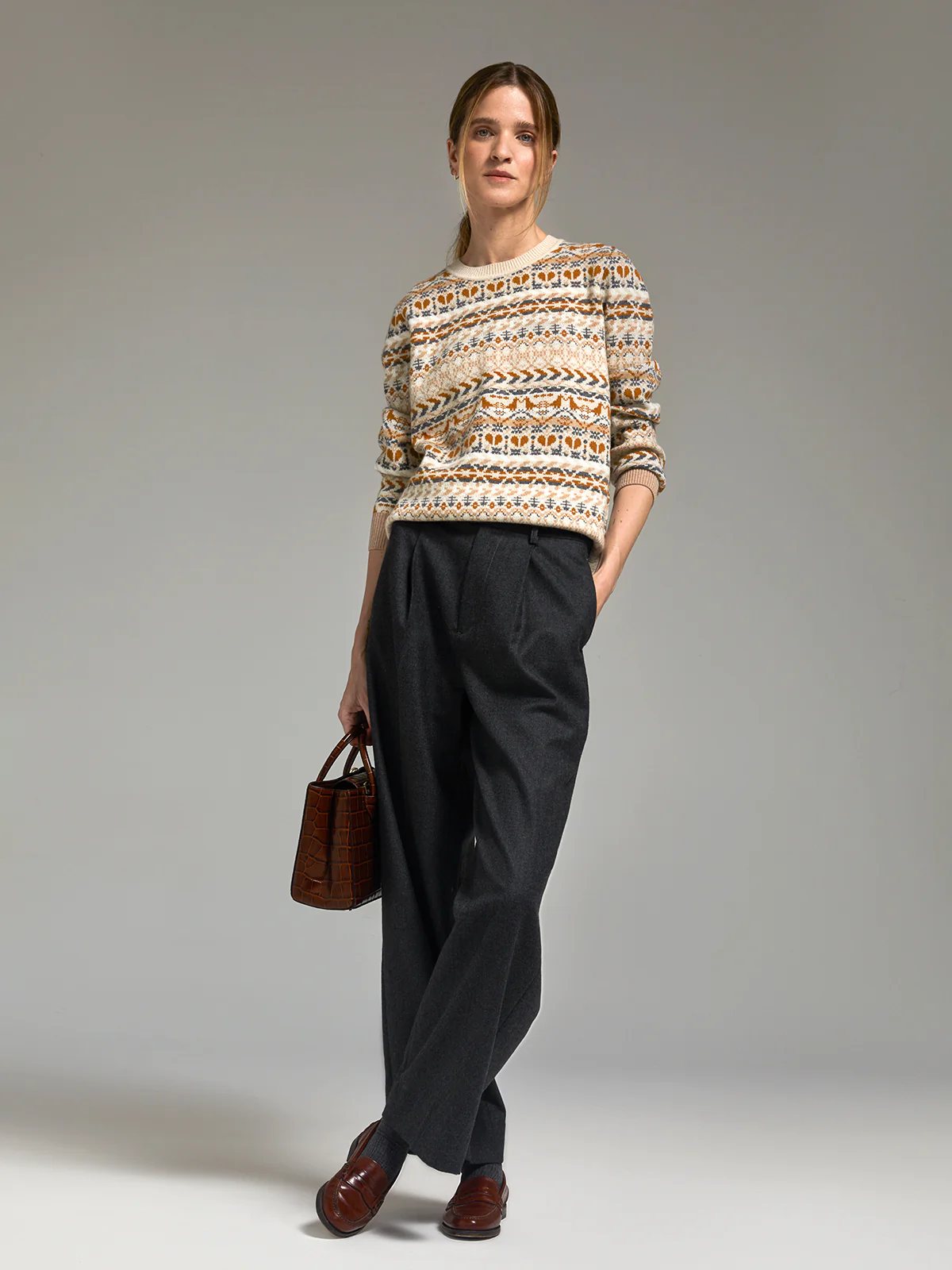Close front view of Gray fine wool wide-leg trousers with pleats, belt, and hands in pockets.
