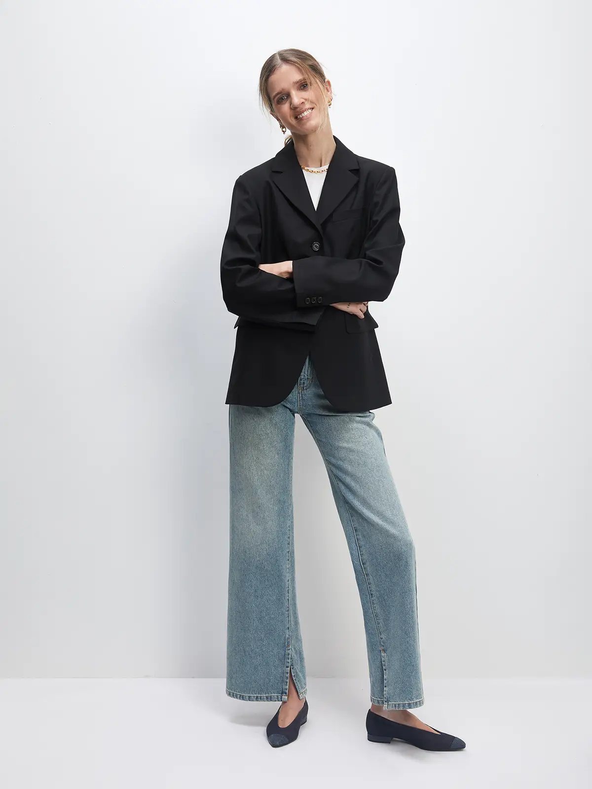 Model in blue retro washed split flared jeans with blazer, top, and flats, front pose with arms crossed.