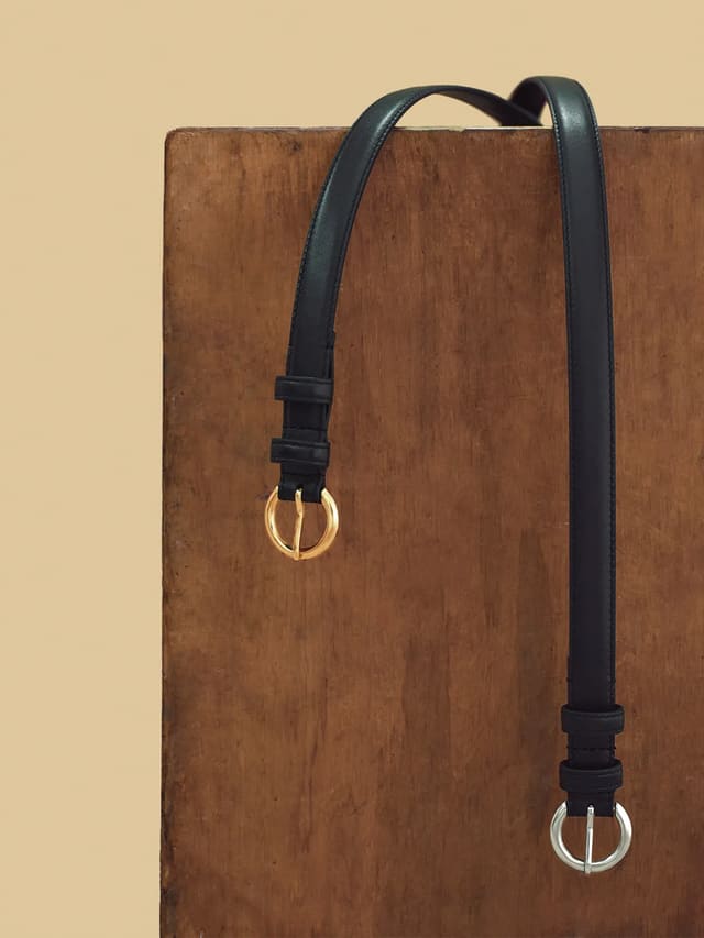 Black and silver KAY belts draped over rustic wooden surface, contrasting finishes side by side