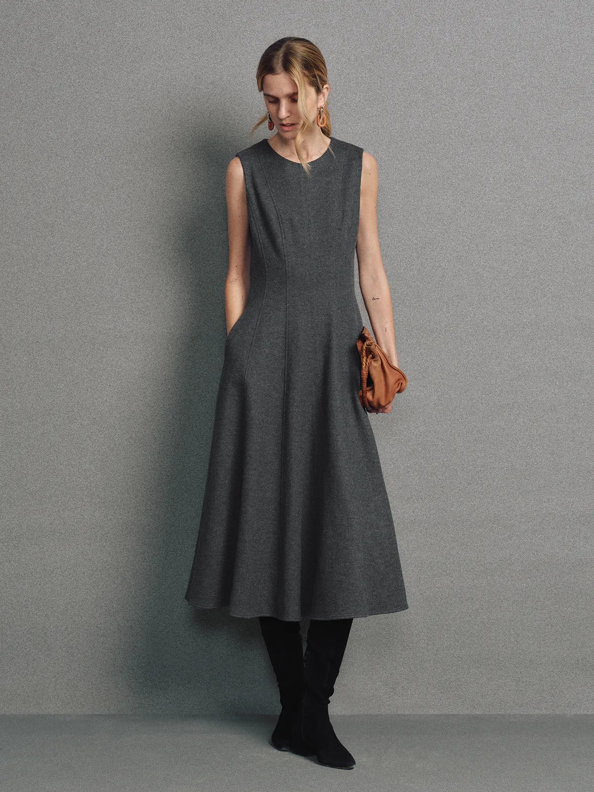 Side view of model in a sleeveless dark gray wool knit A-line dress with boots under directional lighting.