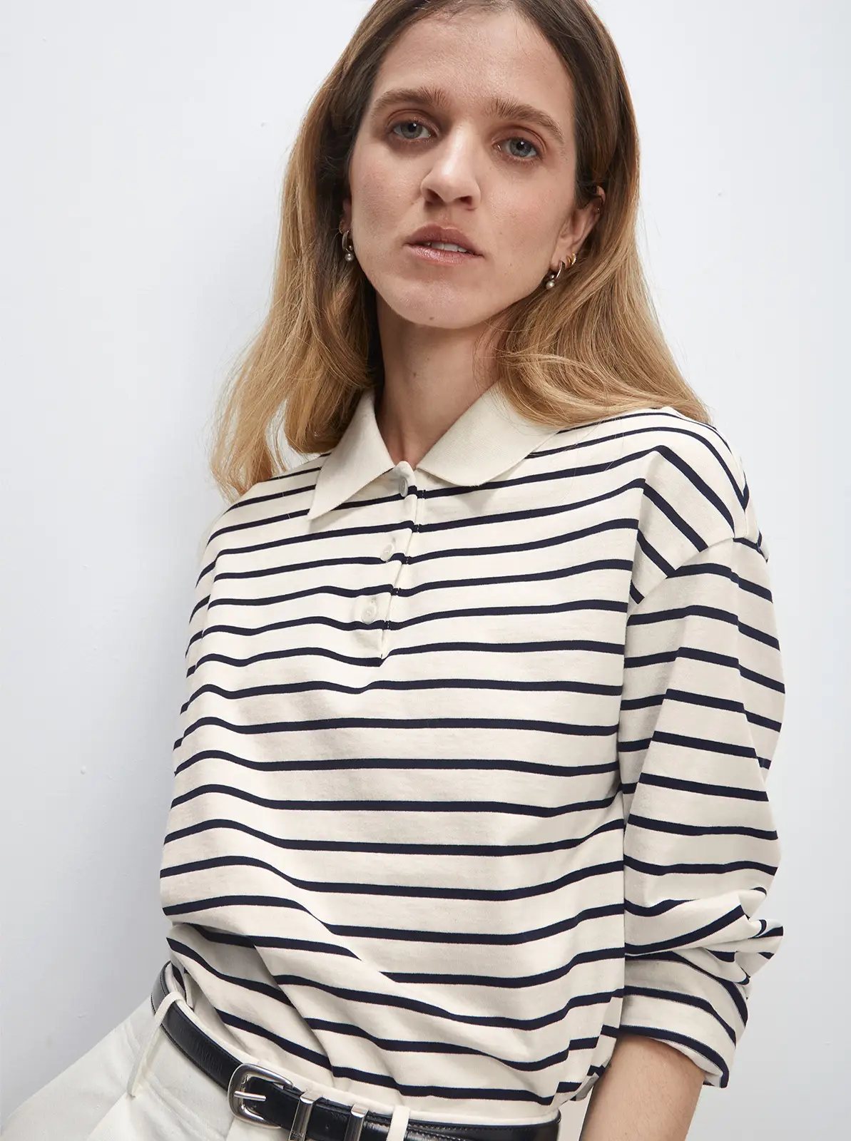 Close-up of a model in a white/black striped long-sleeve polo collar cotton t-shirt with a collar and black belt.