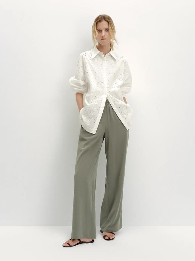 Model wearing PATRICIA wide-leg trousers with white embroidered eyelet shirt and flat sandals