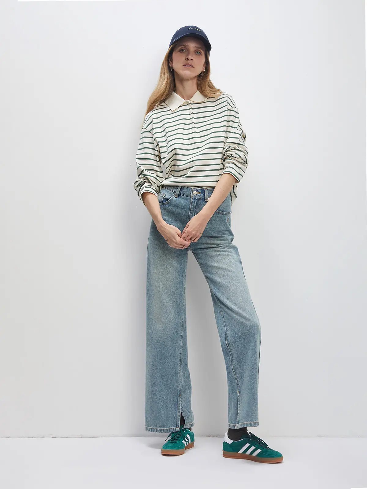 Model wearing a white/green striped long-sleeve polo collar cotton t-shirt with jeans, green sneakers, and a cap.