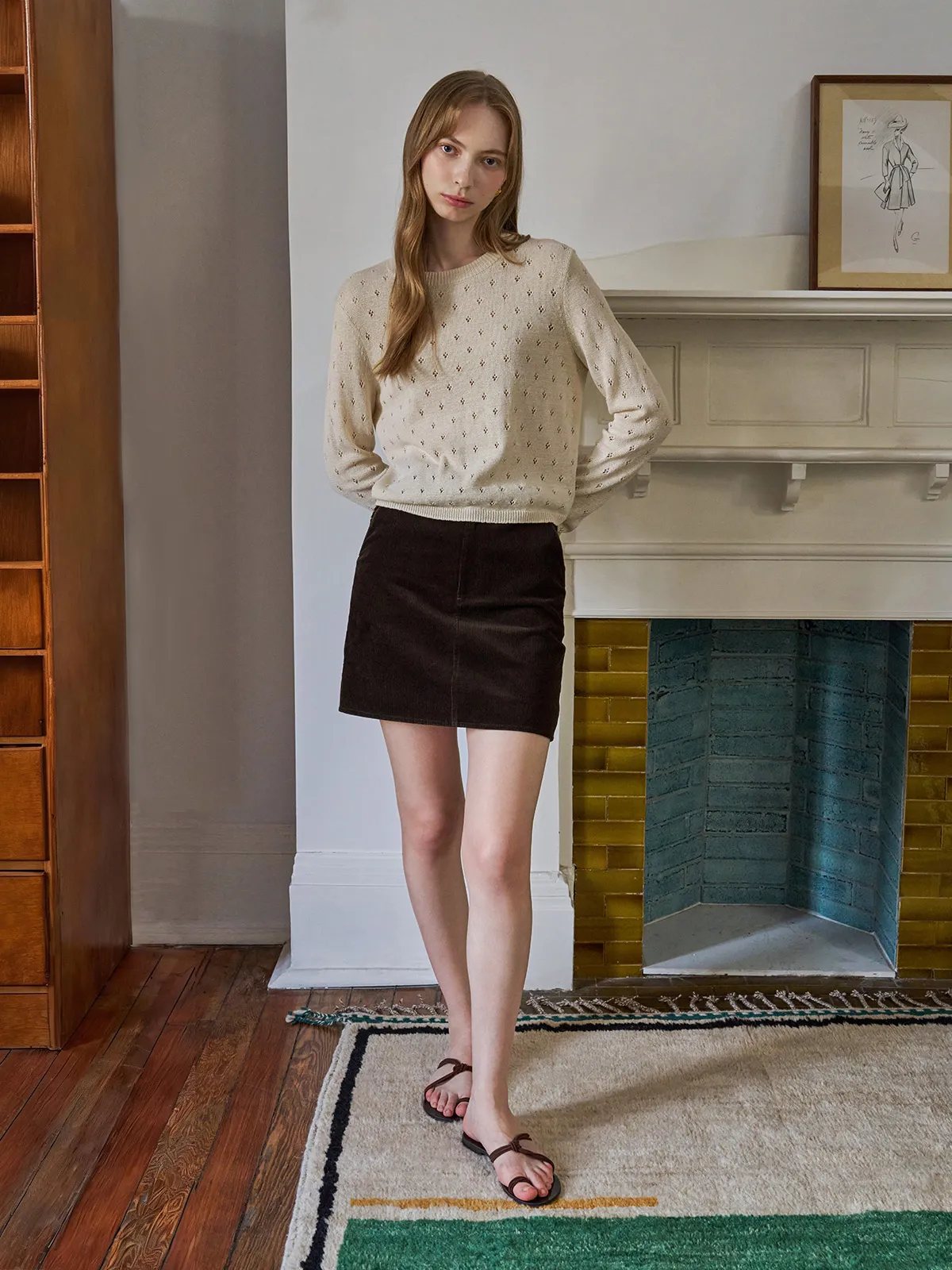 Full-length side view of model in KIANA top and brown corduroy skirt on patterned rug