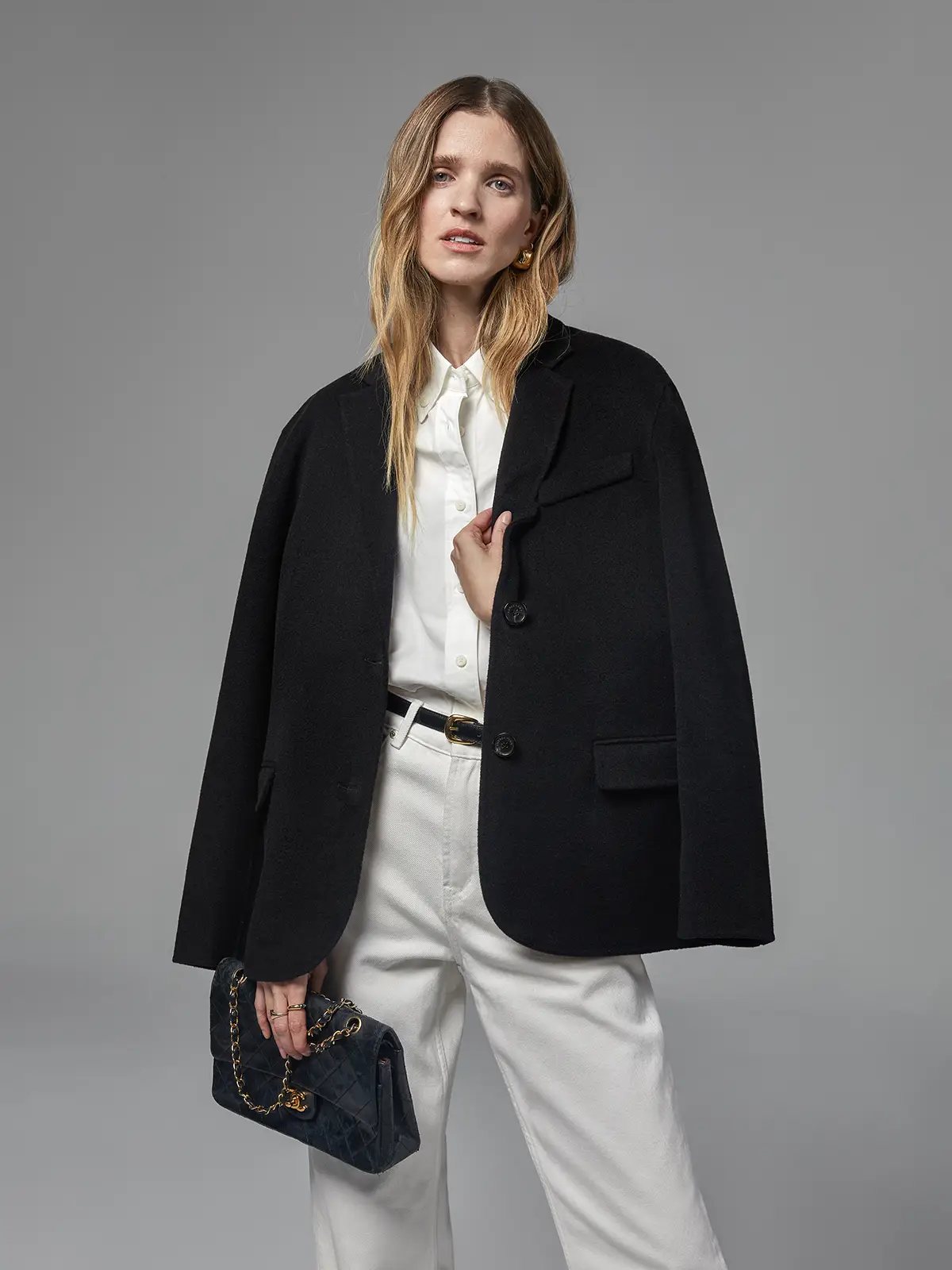 Close-up of model wearing a Black merino wool blazer with shirt, pants, and a dark handbag.