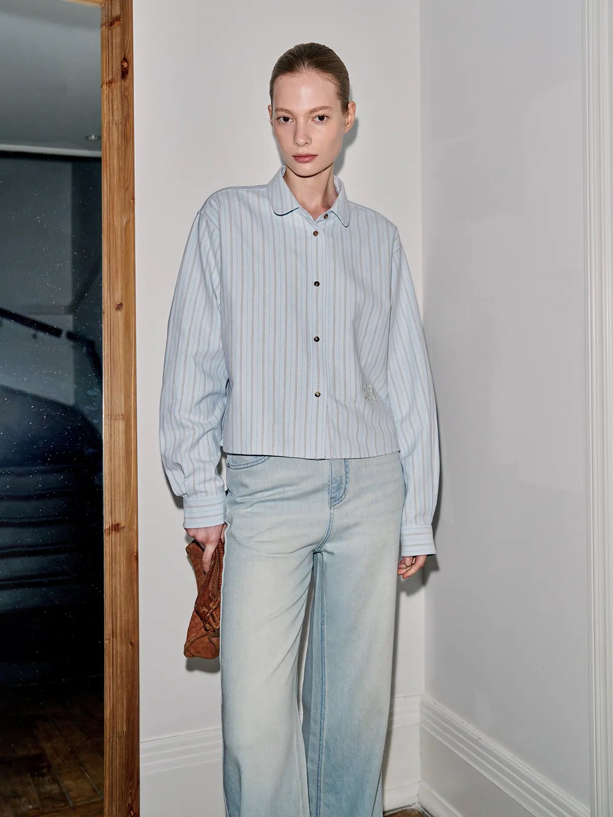 Model in side profile wearing PIXIE shirt with light-wash wide-leg jeans and holding leather clutch