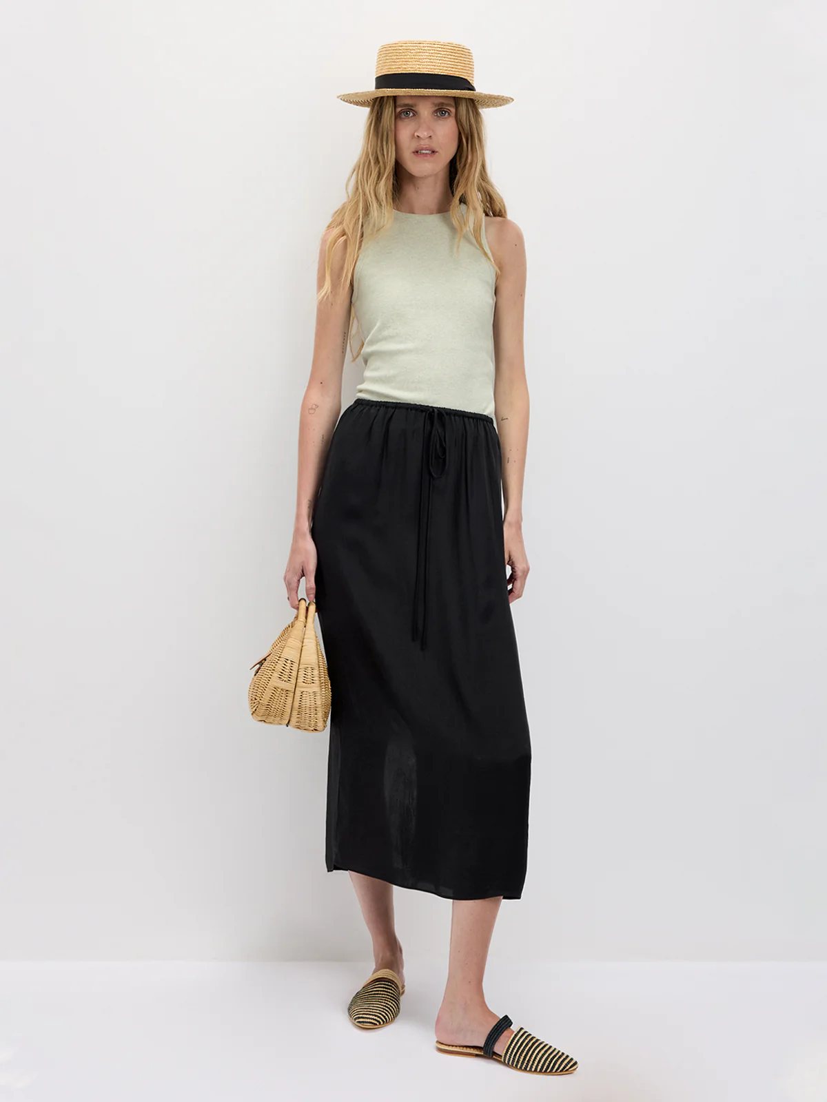 Model in a Light green fitted tank top with a midi skirt, straw hat, and woven bag, front view.