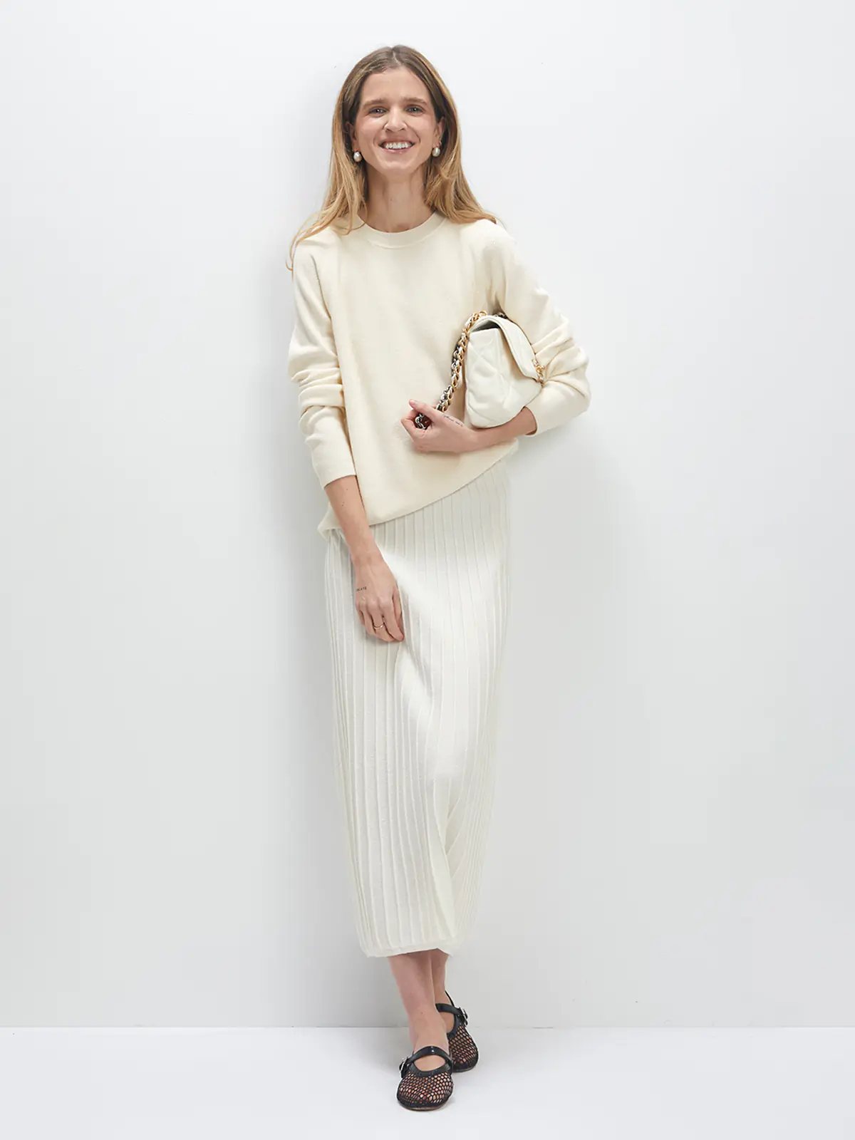 Model wears the white JOCELYN dress under a sweater, holding a clutch and wearing mesh flats.