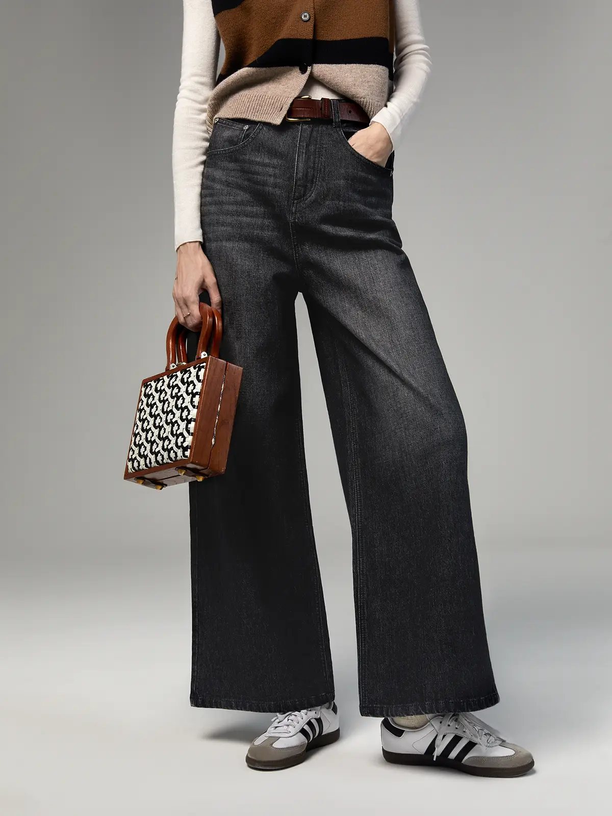 Close-up of Dark Grey wide-leg jeans paired with a striped vest, belt, and patterned handbag.