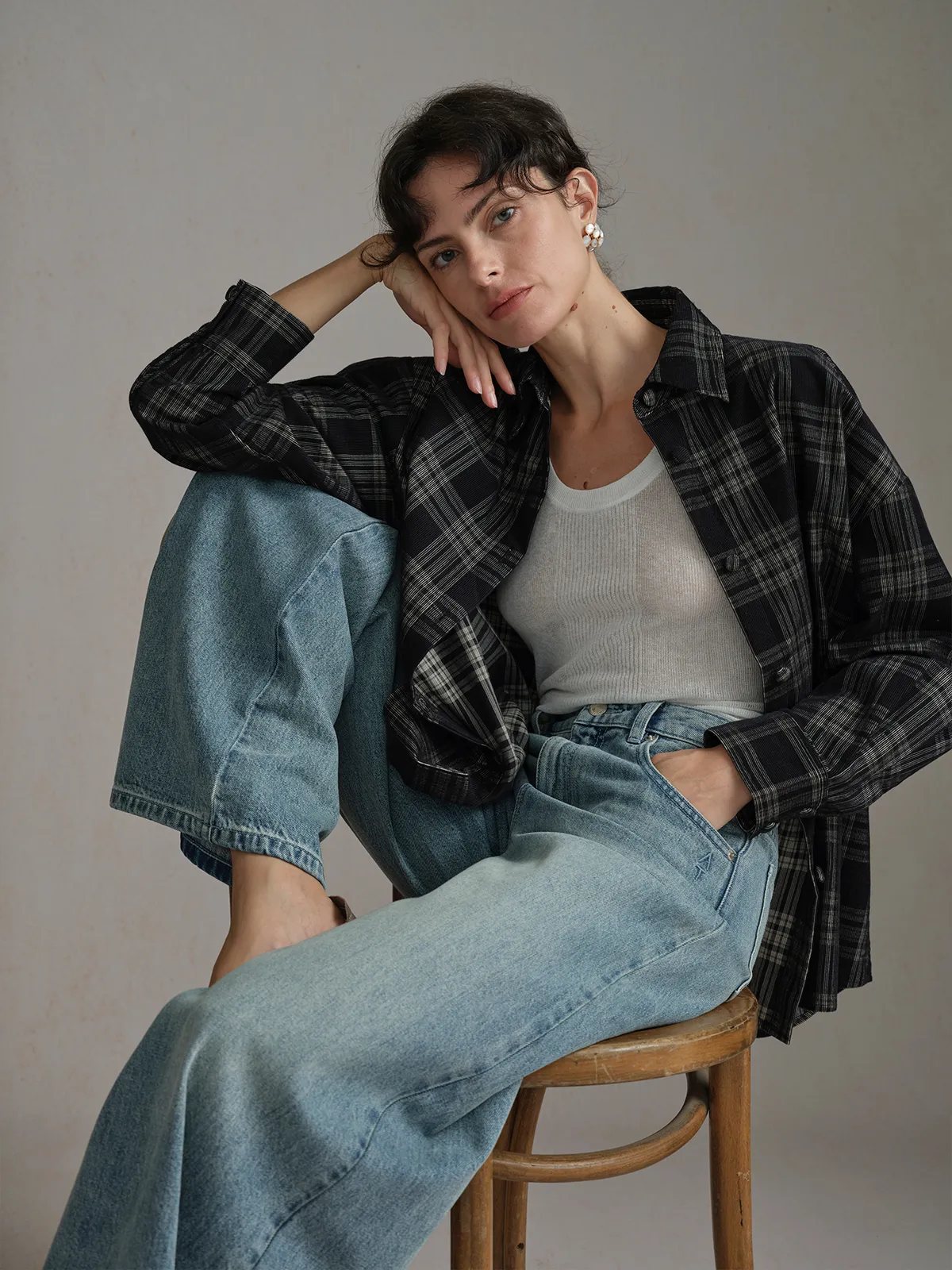 Model seated on wooden stool wearing ALDER corduroy overshirt layered over white tank, one hand resting on cheek