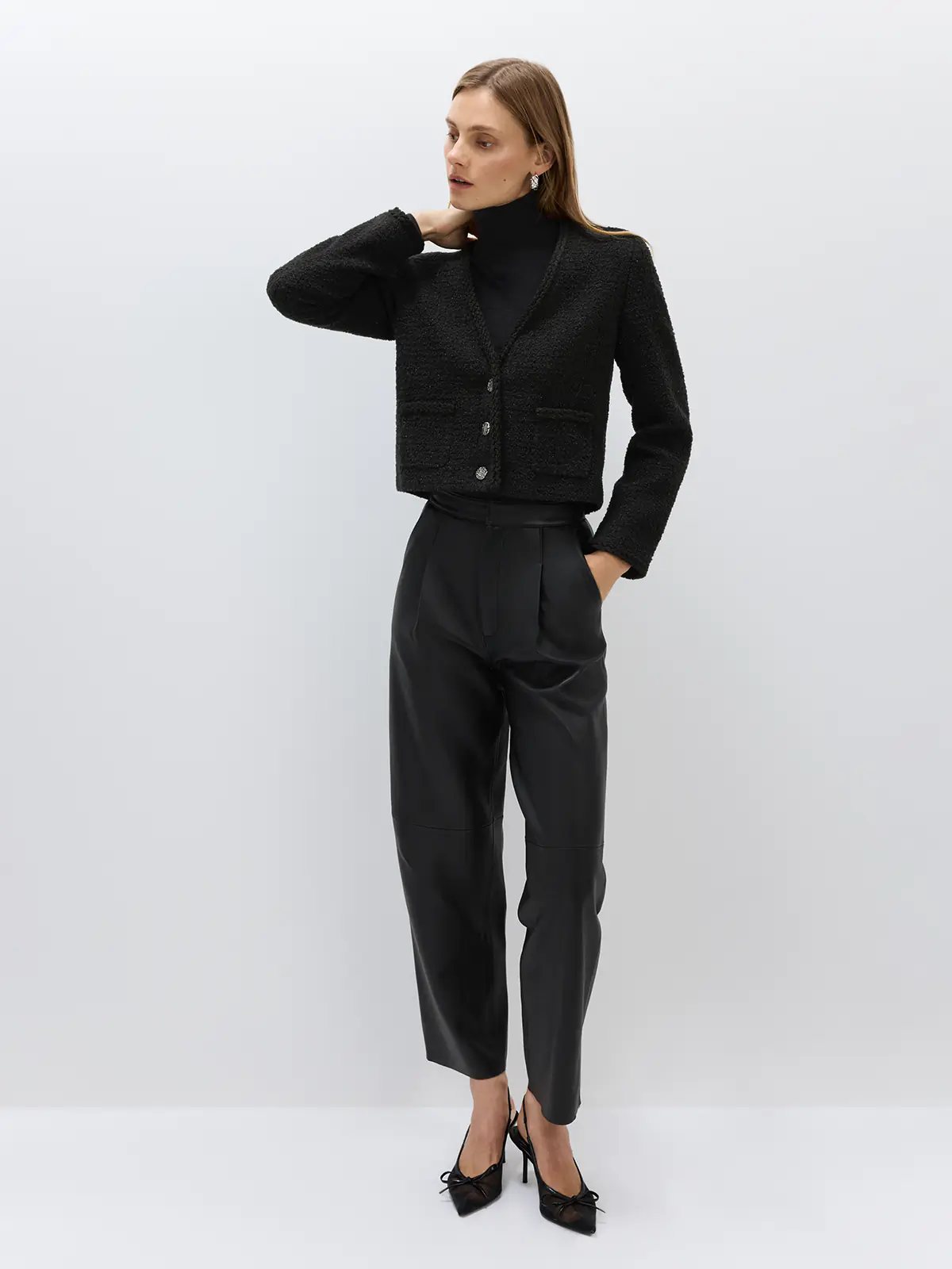 Side view of black sheepskin leather casual pants styled with a coat, sweater, bag, and sneakers.