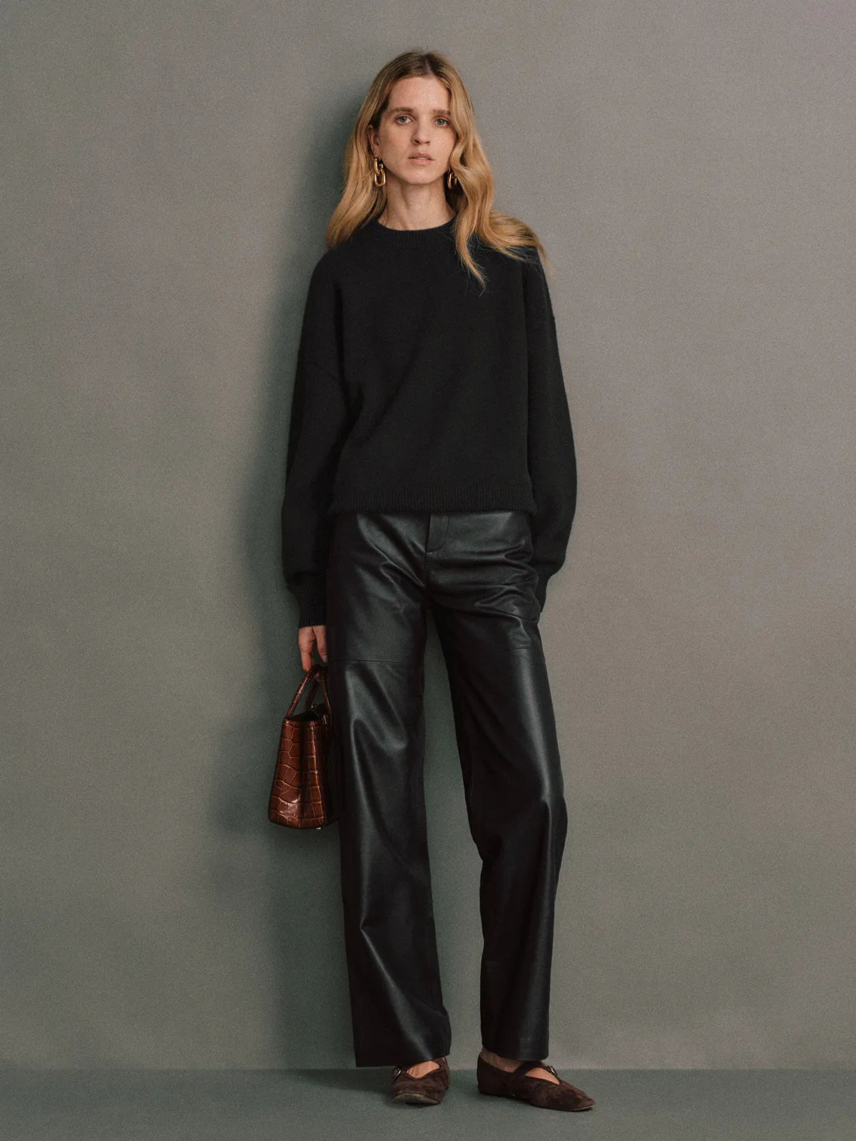 Front view of a model wearing Black soft leather straight trousers with a black sweater and flats.