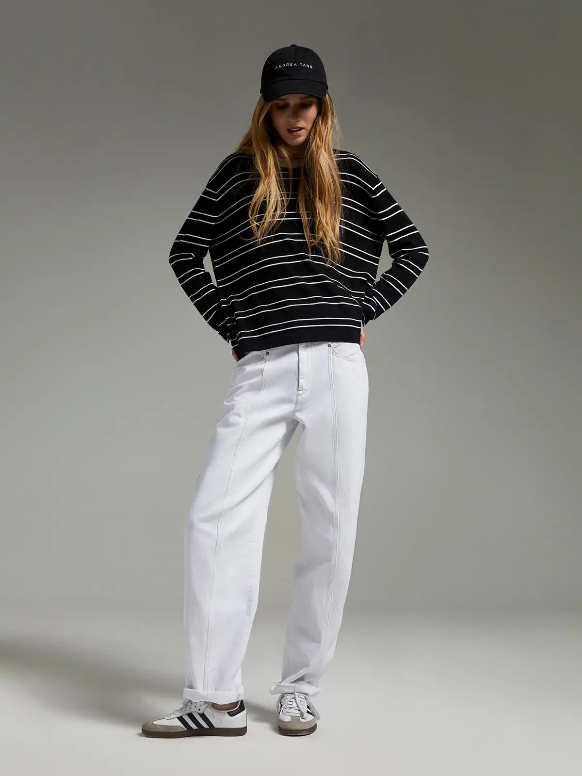 Model wearing a black striped knit top with horizontal stripes, paired with pants and a black cap.