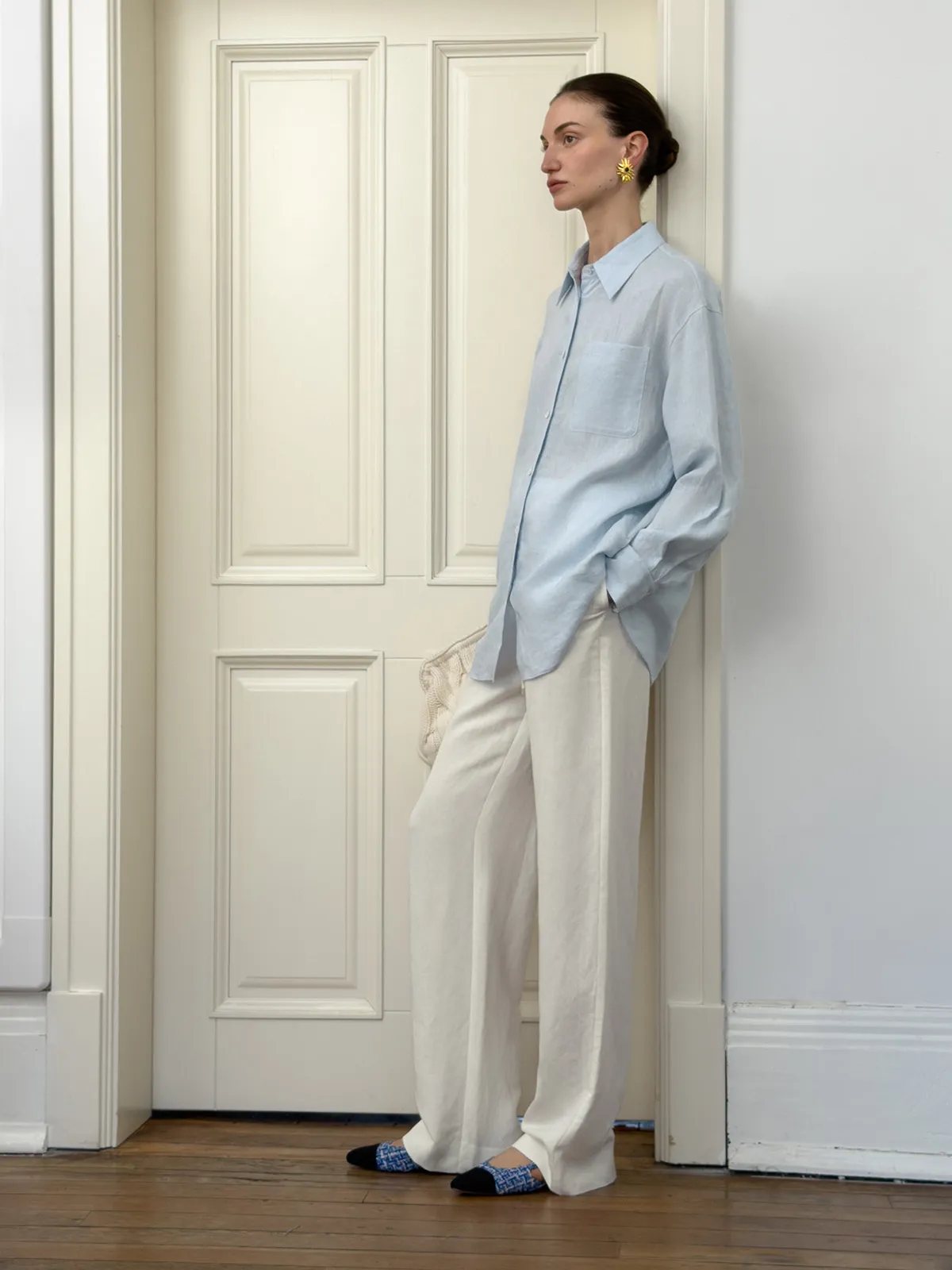 Side profile of model in ivory linen wide-leg trousers with light blue linen shirt and patterned flats