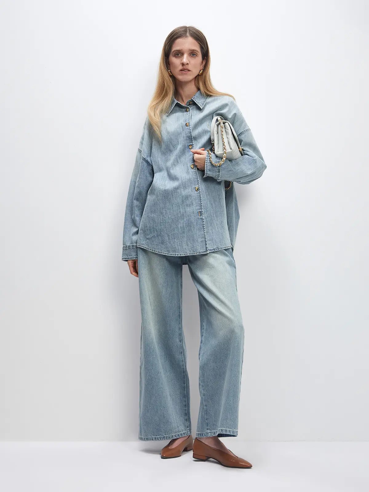 Model wears a light blue oversized denim shirt with button front and relaxed fit, paired with matching wide-leg jeans.