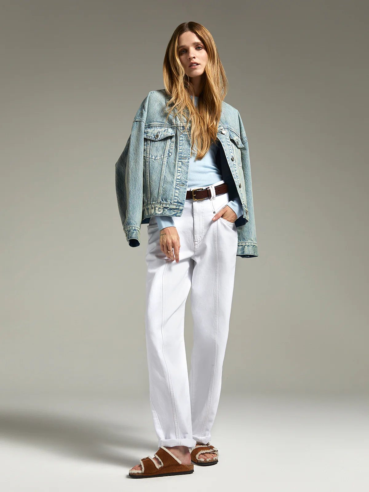 Model in andreatang light-blue vintage-wash denim jacket with logo hem, pale blue knit and white jeans