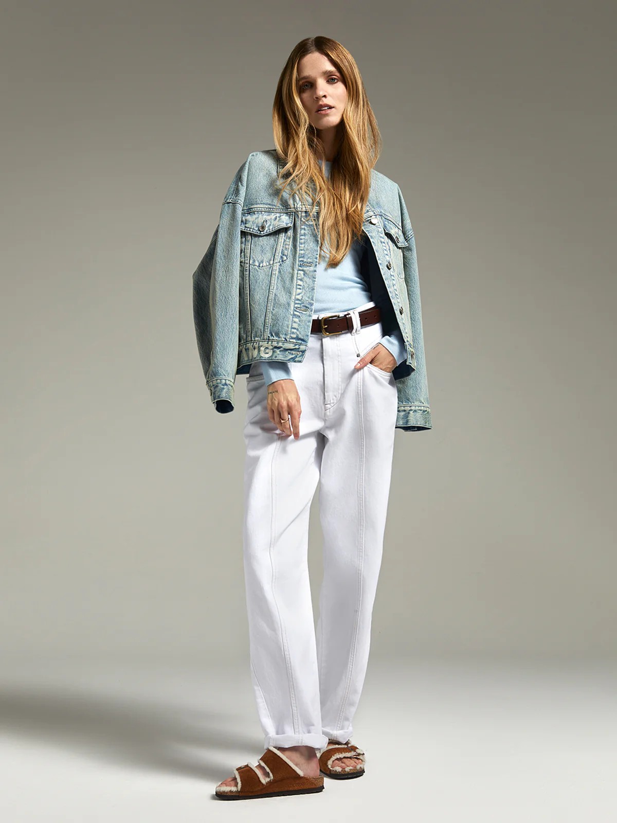 Model in andreatang light-blue vintage-wash denim jacket with logo hem, pale blue knit and white jeans