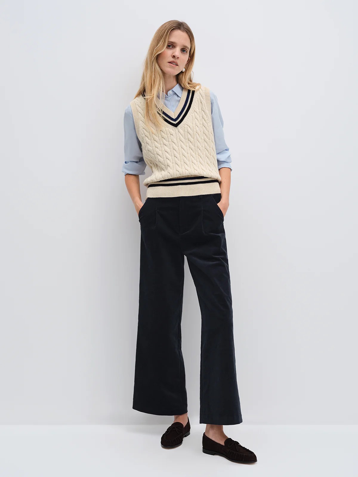 andreatang cable-knit cricket vest layered over light blue shirt with wide-leg navy trousers