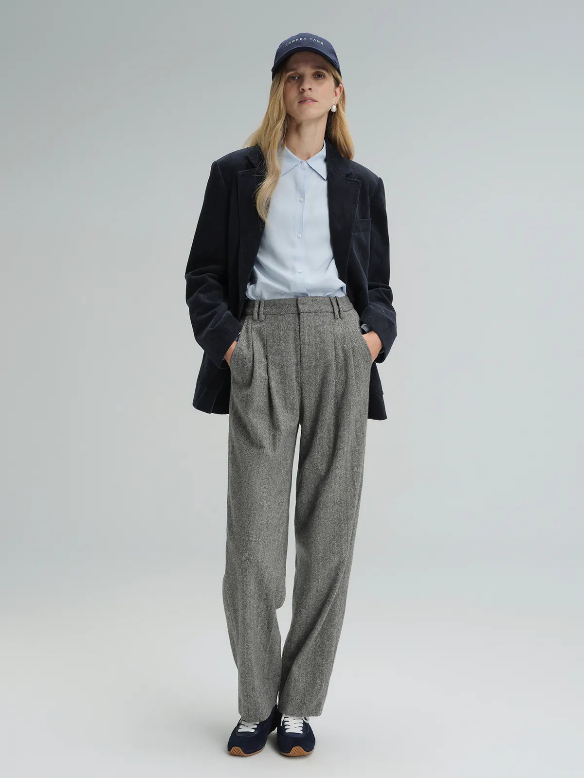 Model wearing Gray wool herringbone tapered trousers with hands in pockets, styled under a dark blazer and light shirt.