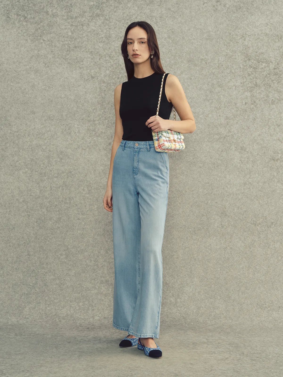 Andreatang LEANNE lightweight lyocell wide leg jeans in stone wash, styled with black sleeveless top and tweed mini bag on model against gray backdrop