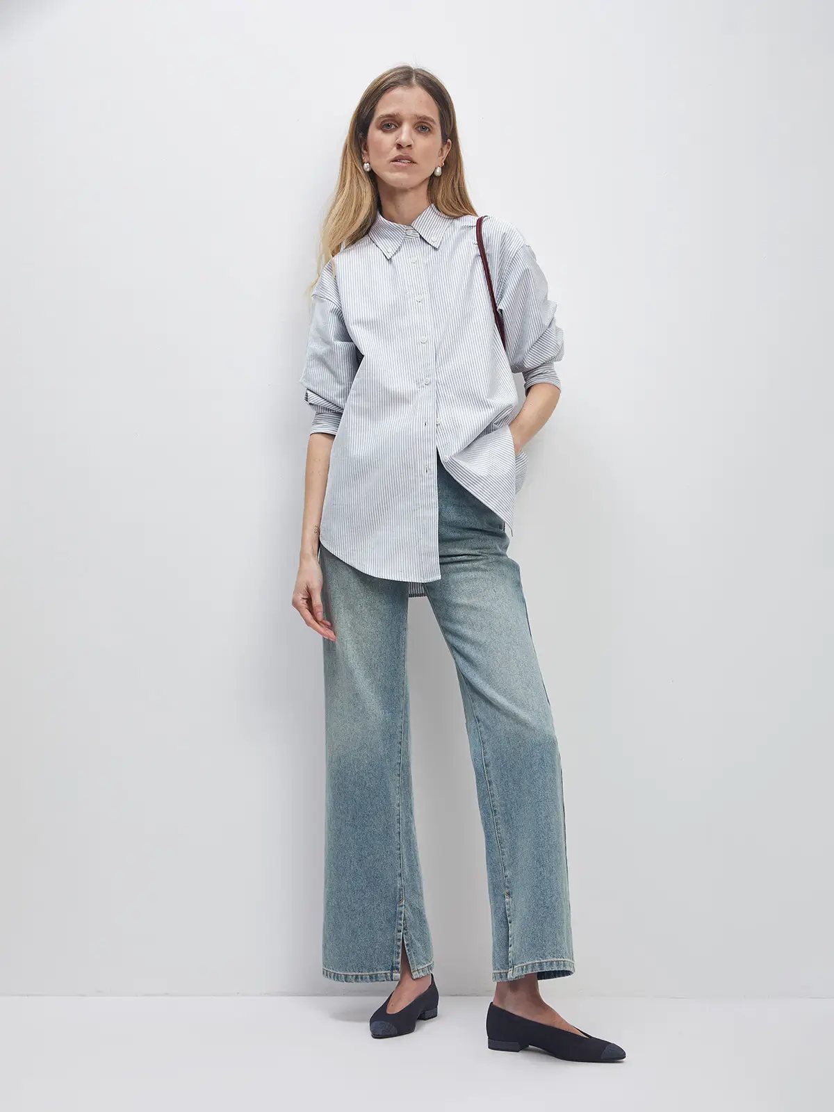 Model in blue retro washed split flared jeans styled with oversized striped shirt and flats, front full-body view.
