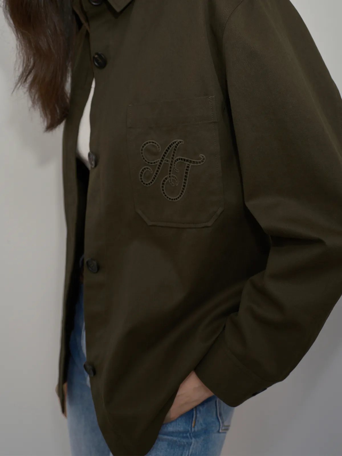 Close-up of openwork embroidered 'AT' monogram on chest pocket of olive jacket