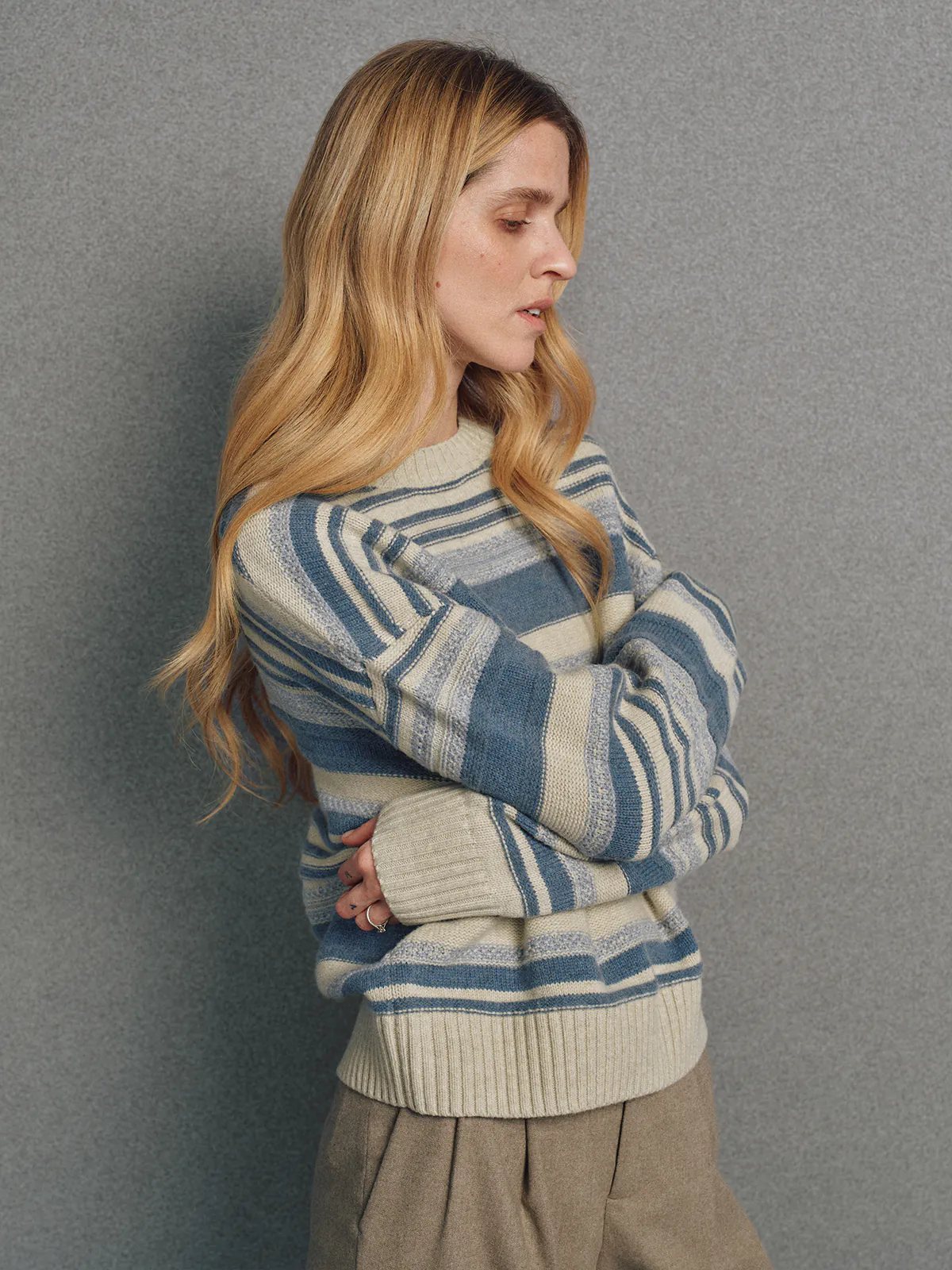 Side view of model in a blue irregular multicolour stripe wool cotton jumper with arms crossed.