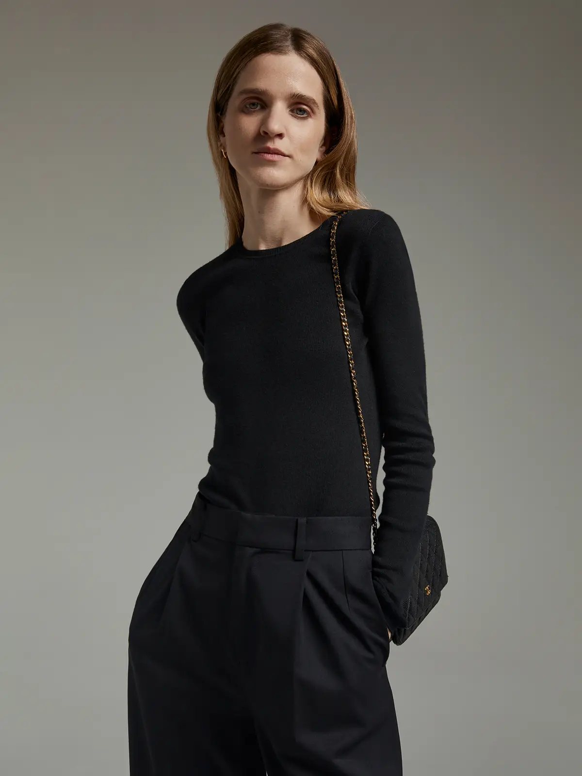 Model in a black slim fit long-sleeve knit top with crew neck and black high-waisted trousers.