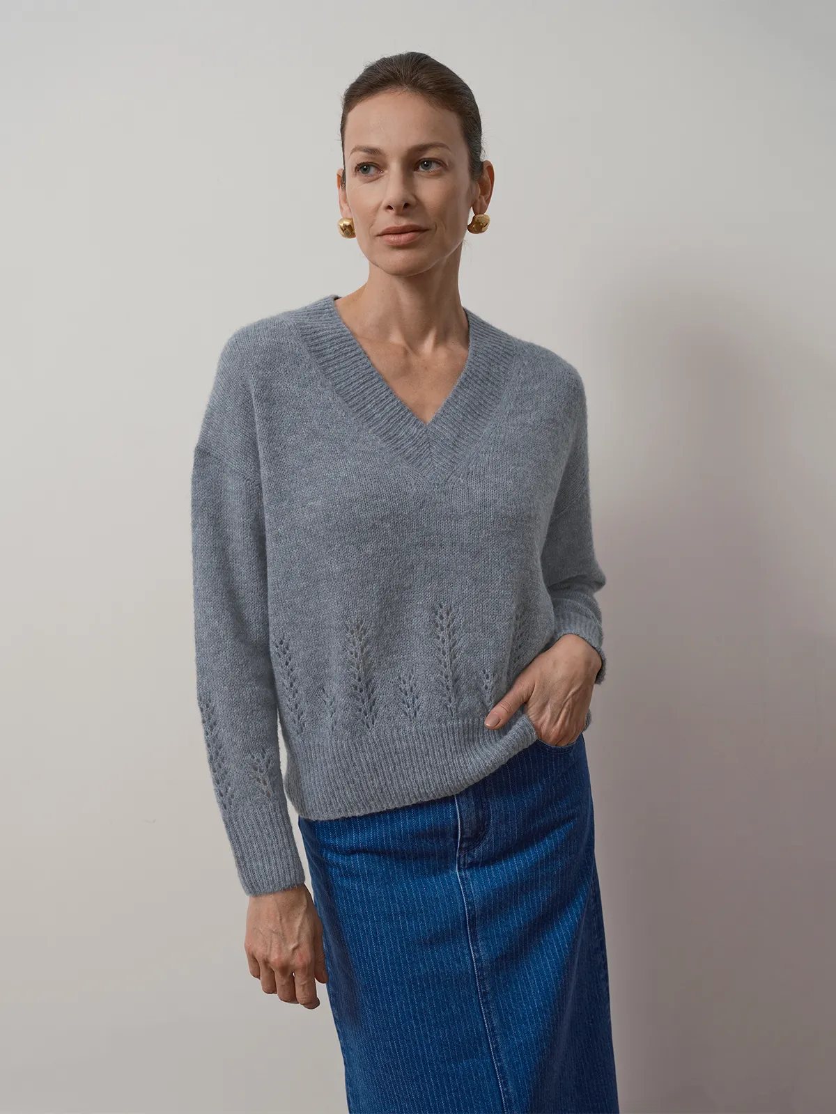 Model wearing dusty blue AIRY Jumper with blue corduroy midi skirt and gold earrings, hand in pocket