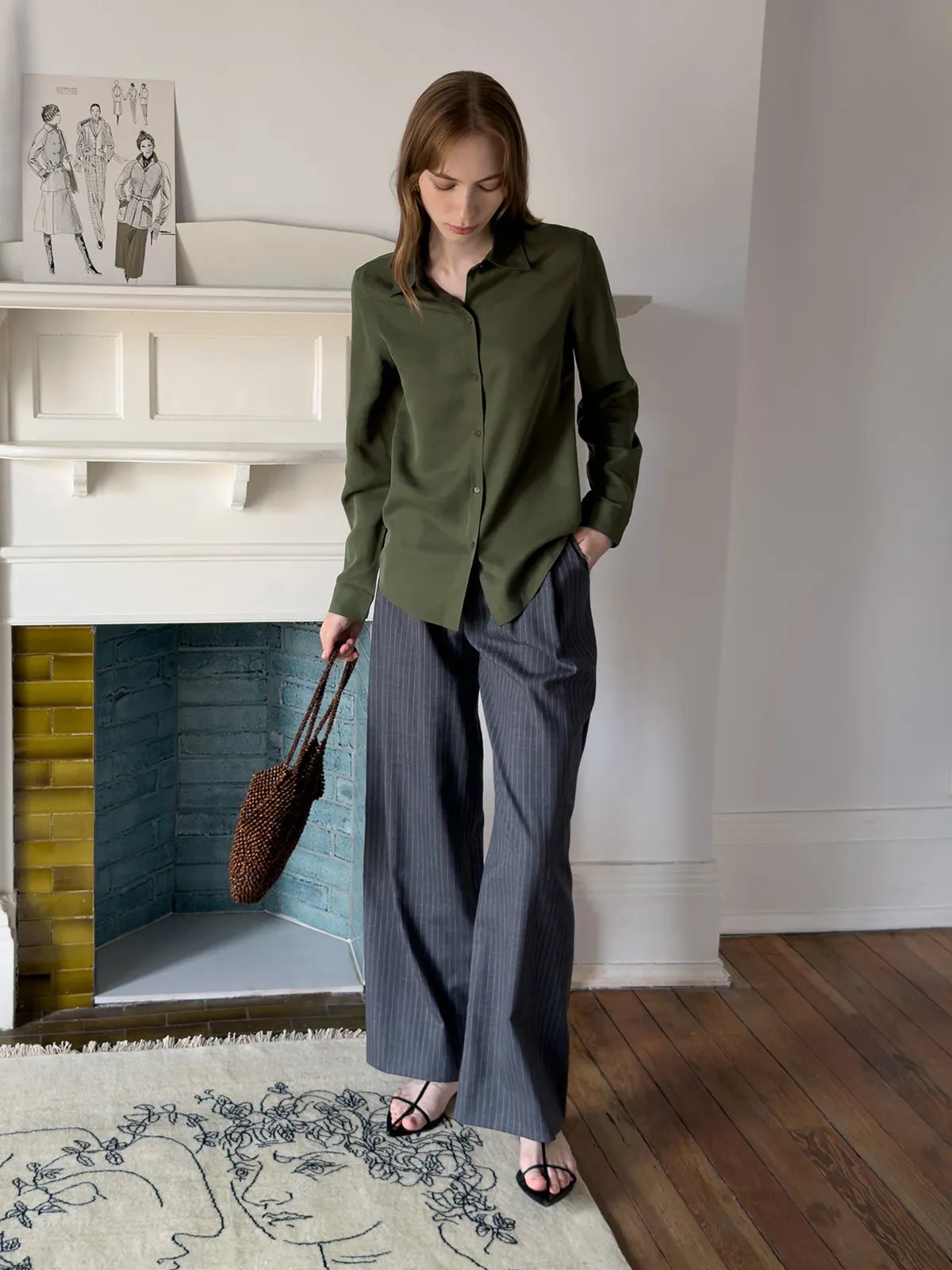Model looking down in ORAN trousers with olive shirt, holding beaded brown tote bag