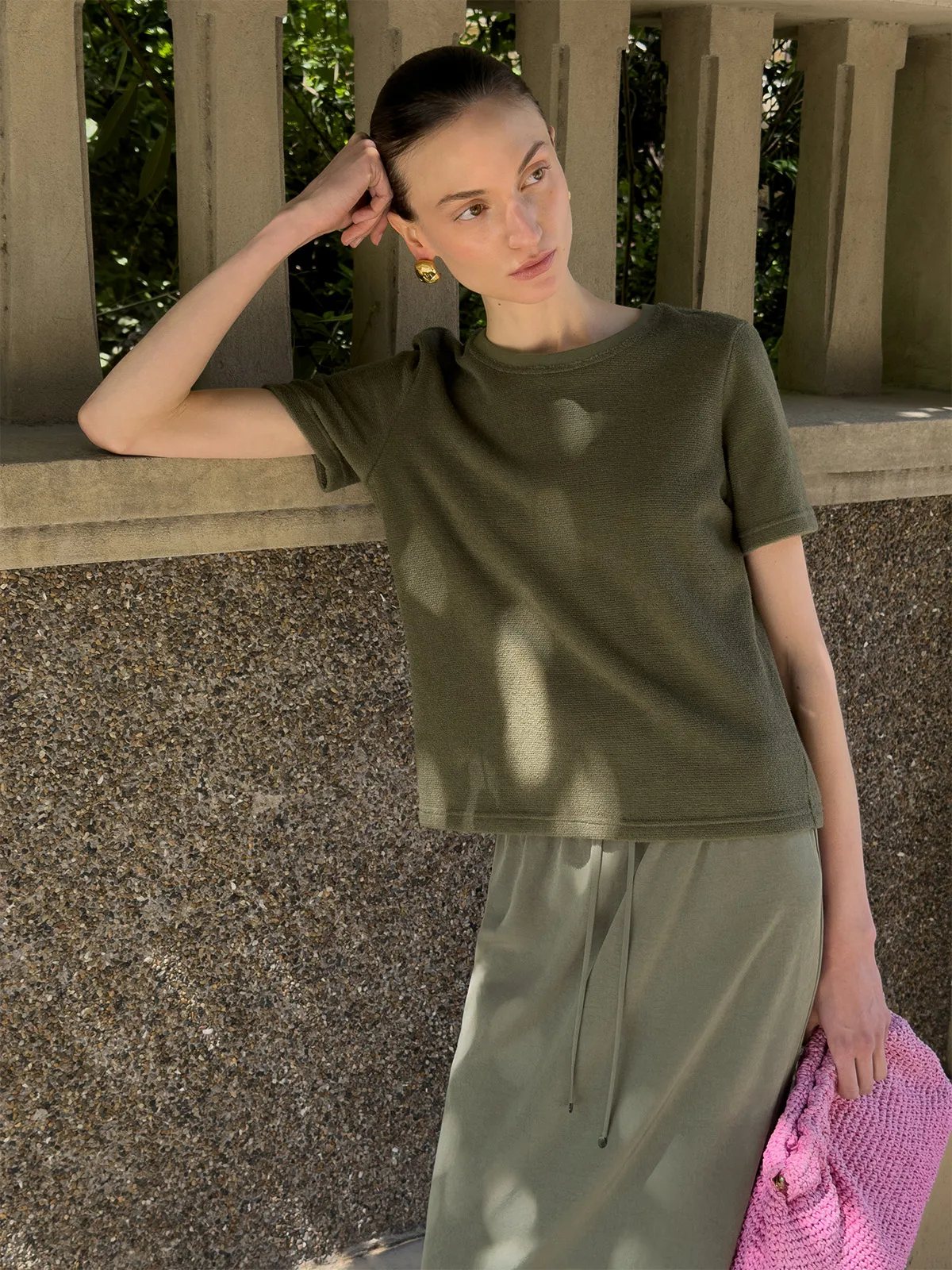Model wearing olive LANE Terry short sleeve t-shirt with matching drawstring skirt, holding pink crocheted bag outdoors
