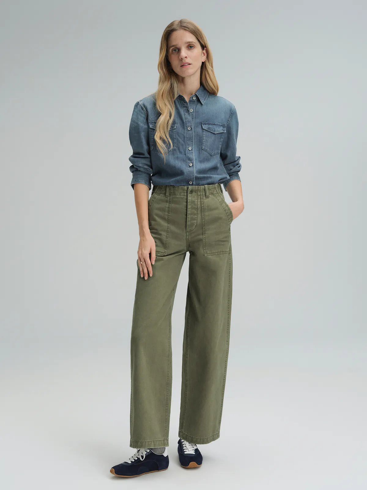 Model wearing olive green cotton utility trousers with wide legs and front patch pockets.
