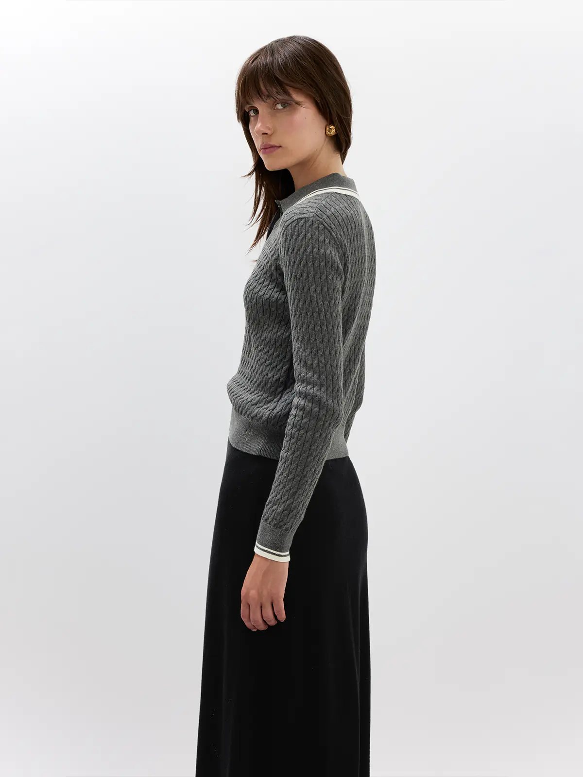 Front view of model in a Grey cable knit polo with long sleeves, ribbed cuffs, and a collar, styled with trousers.
