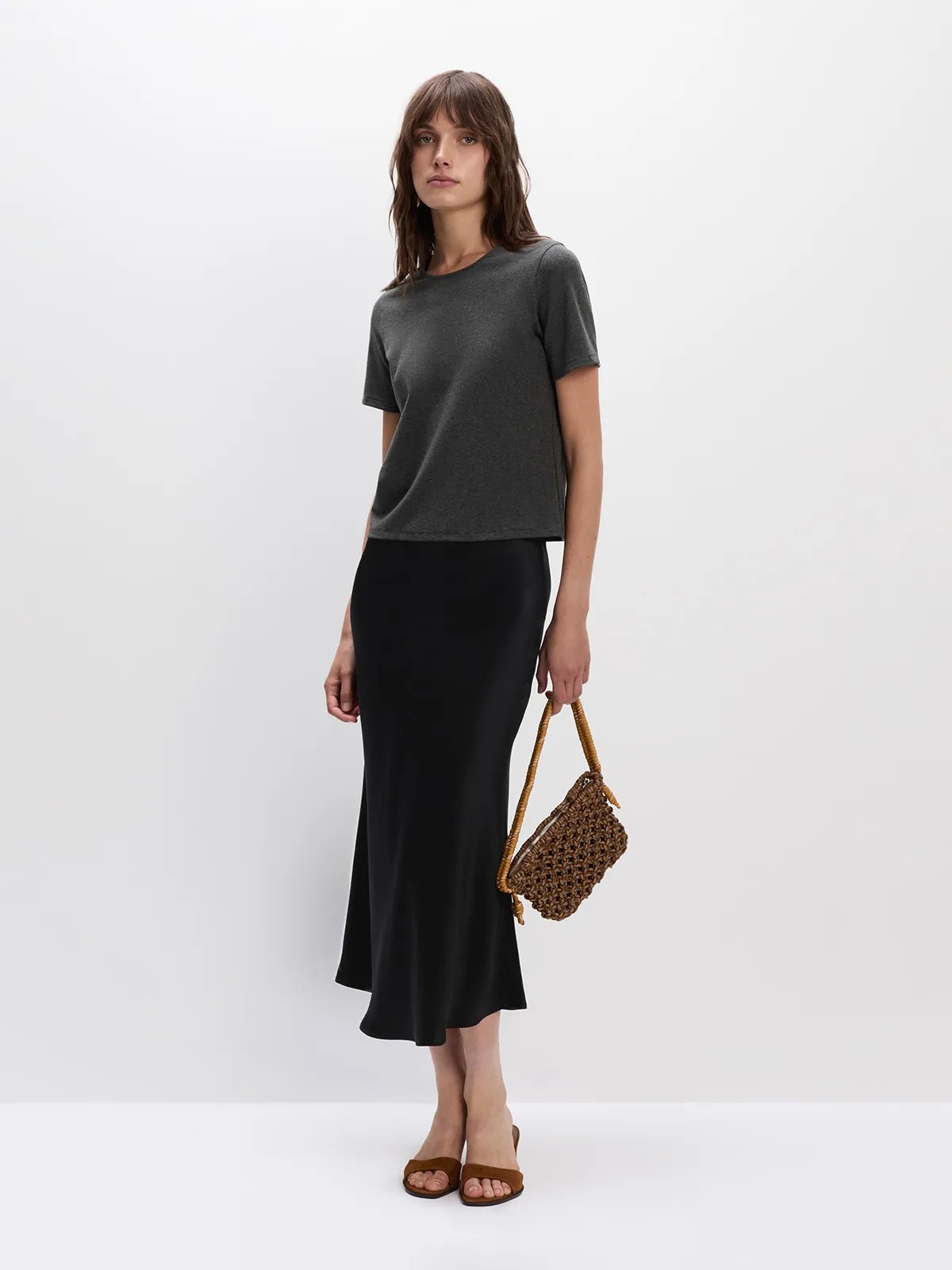 Model in charcoal SOSA t-shirt with black silk midi skirt and woven rattan bag, minimalist evening look