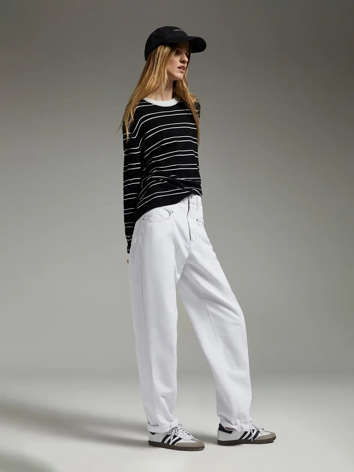 Side view of model wearing a black knit top with horizontal stripes, pants, and a black cap.