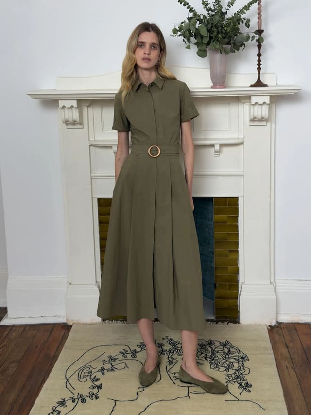 Andreatang IMANI olive green short sleeve shirt dress with wooden ring belt, model standing front view on embroidered rug