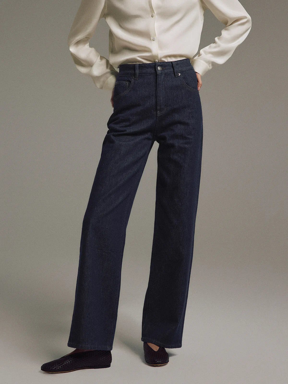 Side pose of model in Blue raw denim straight-leg jeans with a shirt and textured clutch.