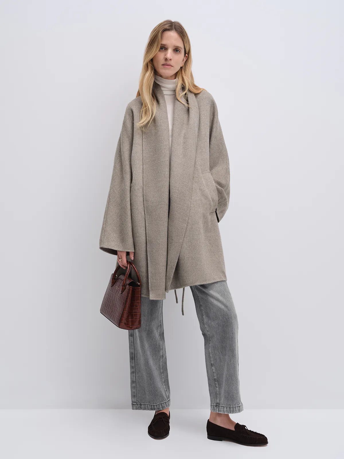 Model wearing a Taupe yak wool robe coat with wide sleeves and front pockets, paired with a turtleneck and jeans.