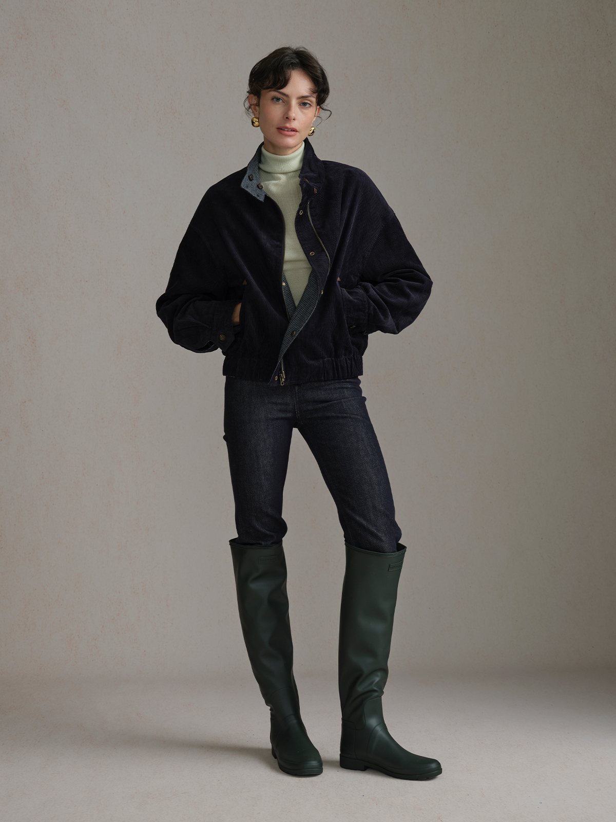 Model wearing the Navy Andreatang CHARLIE jacket, corduroy side out, with a light high-neck top, dark jeans and tall green boots.