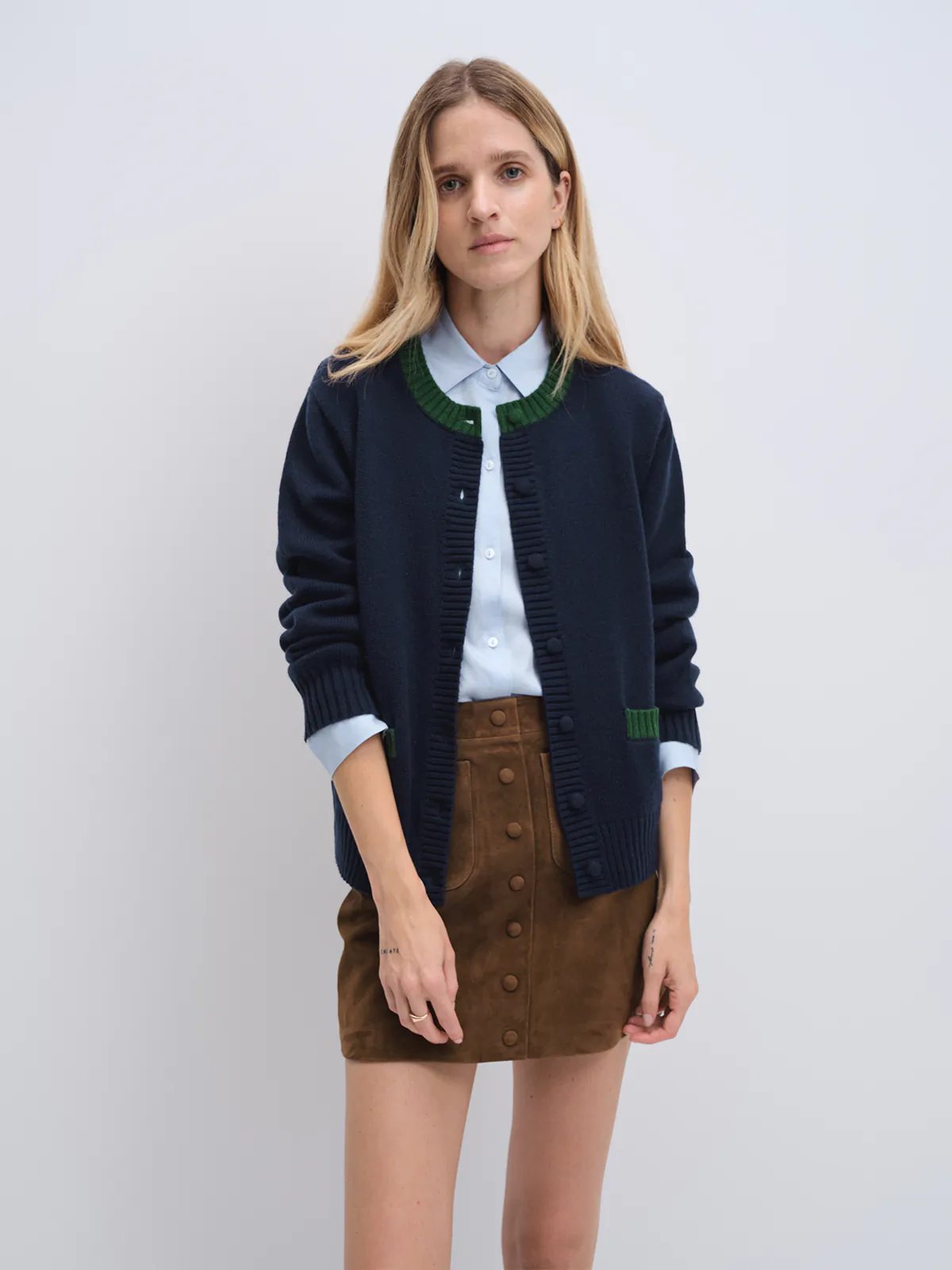 Front view of model in navy cardigan with contrast trim at collar and pocket edges, layered over a light shirt.