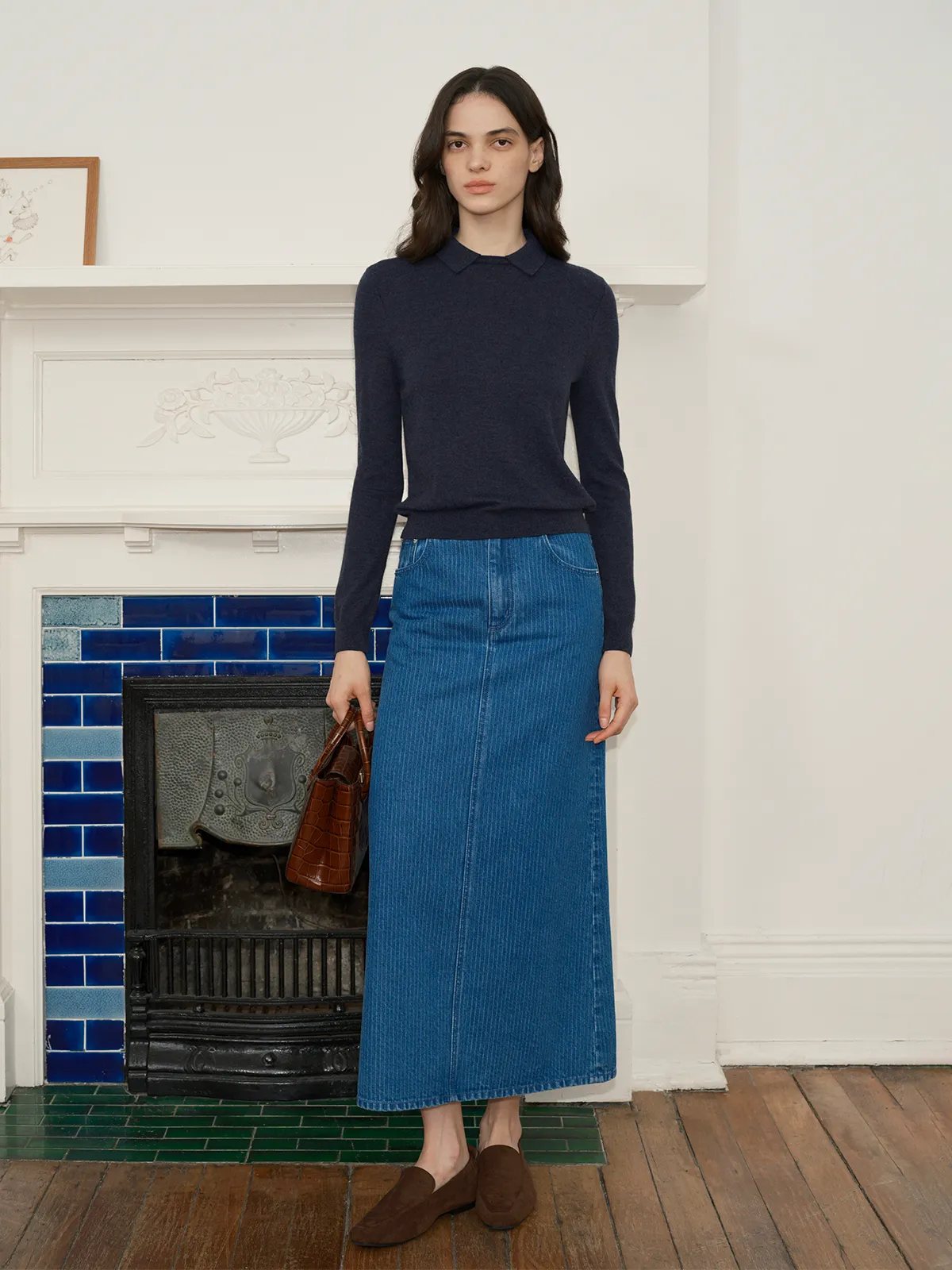 andreatang LOUANE Layered Collar Jumper in navy blue worn with blue corduroy midi skirt and brown leather bag against white fireplace