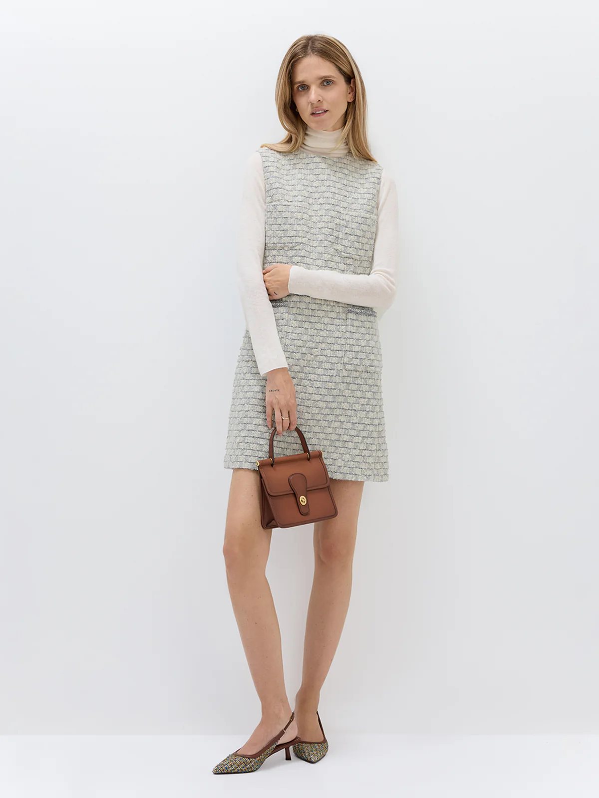 Front view of model in andreatang bouclé check sleeveless mini dress with ivory turtleneck and slingback heels