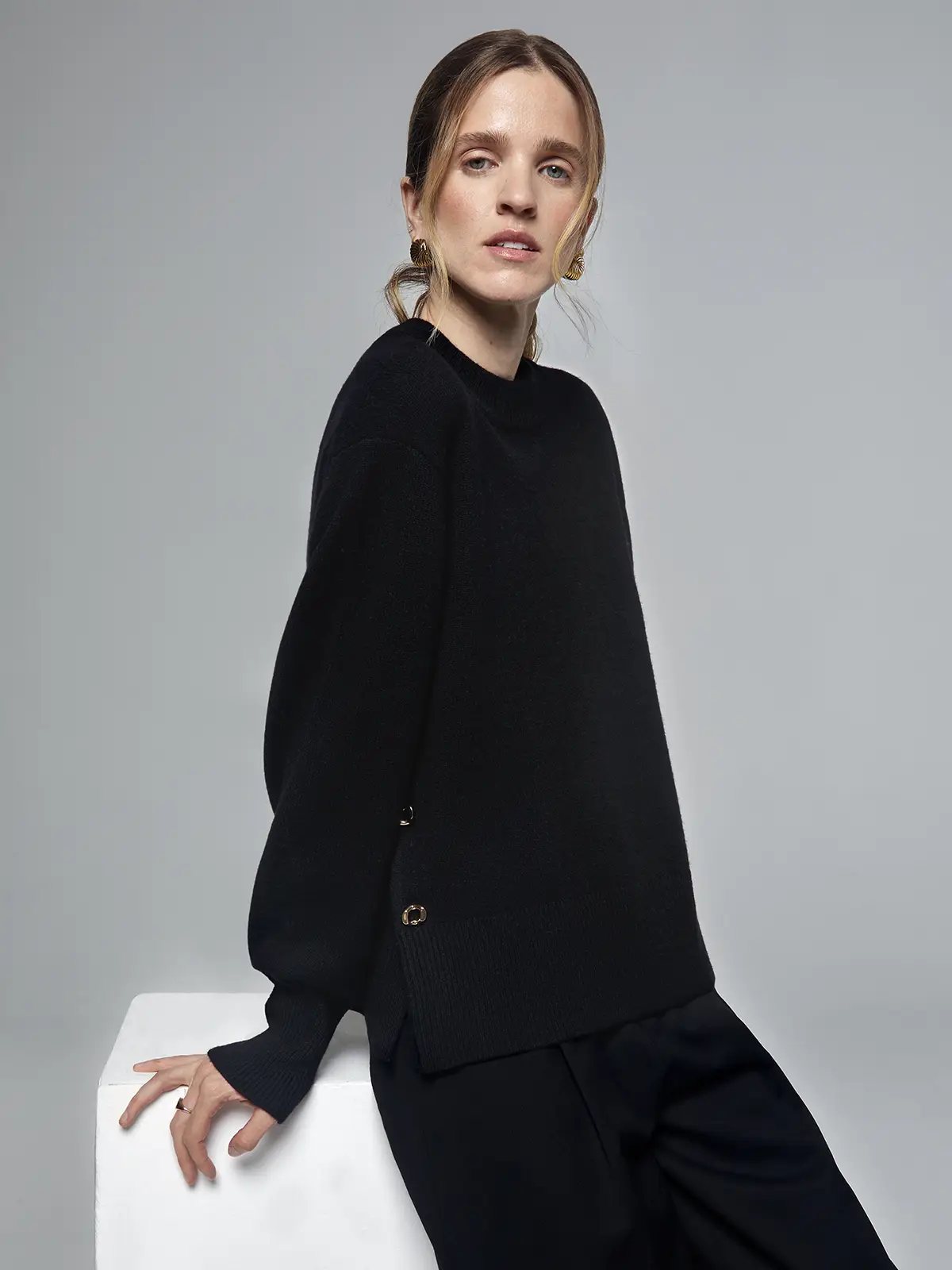Close-up of a black merino wool sweater showing metal button detail on the side seam and ribbed hem.