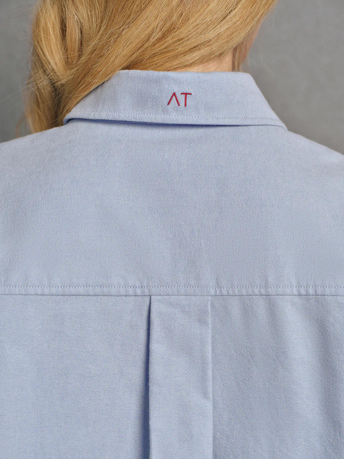 Close-up of the collar and placket of a Blue brushed oxford shirt showing buttons and small contrast embroidery detail.