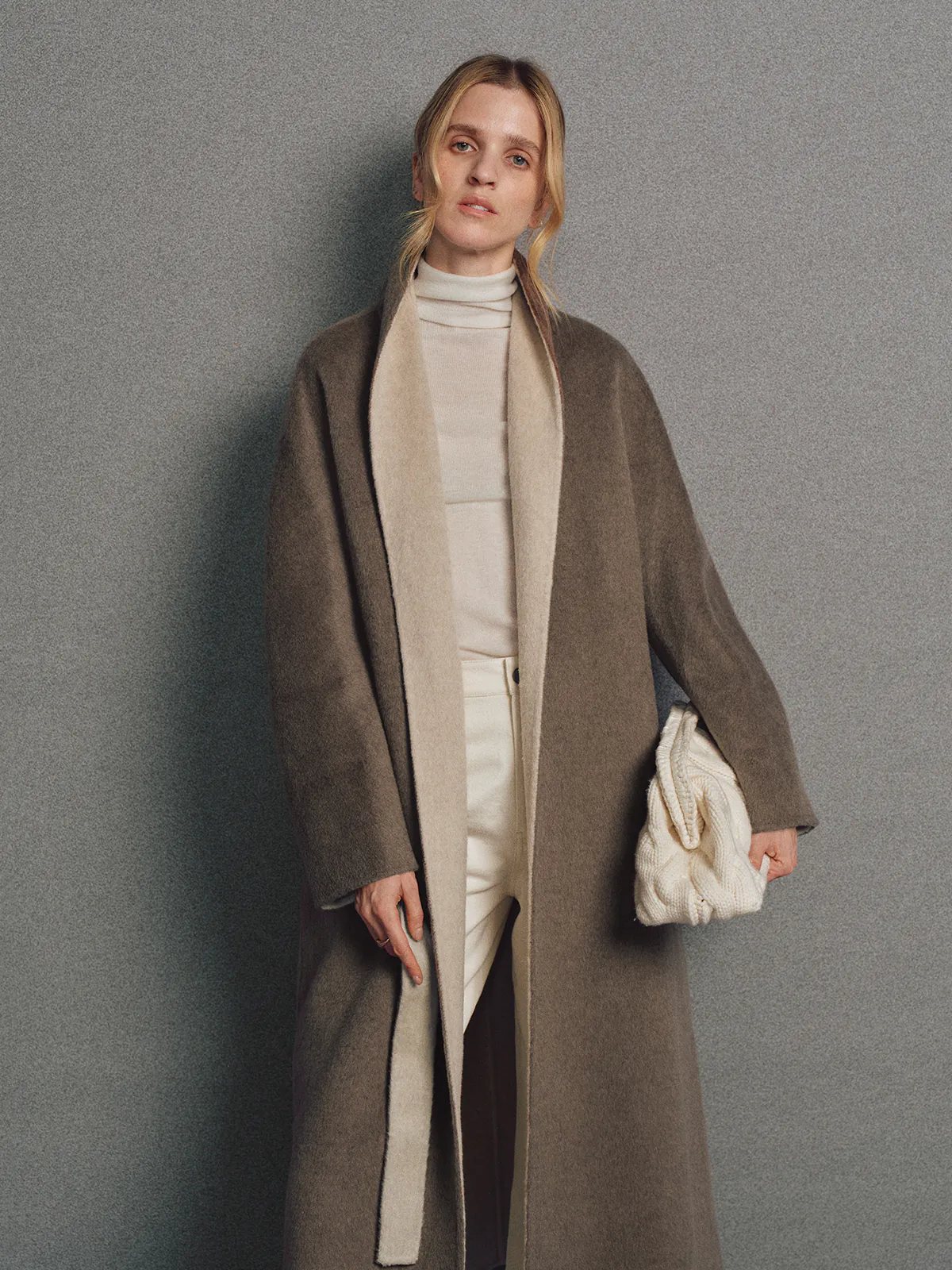 Model in brown two-tone reversible notched-collar coat with lapel and belt, wearing cap and sneakers.