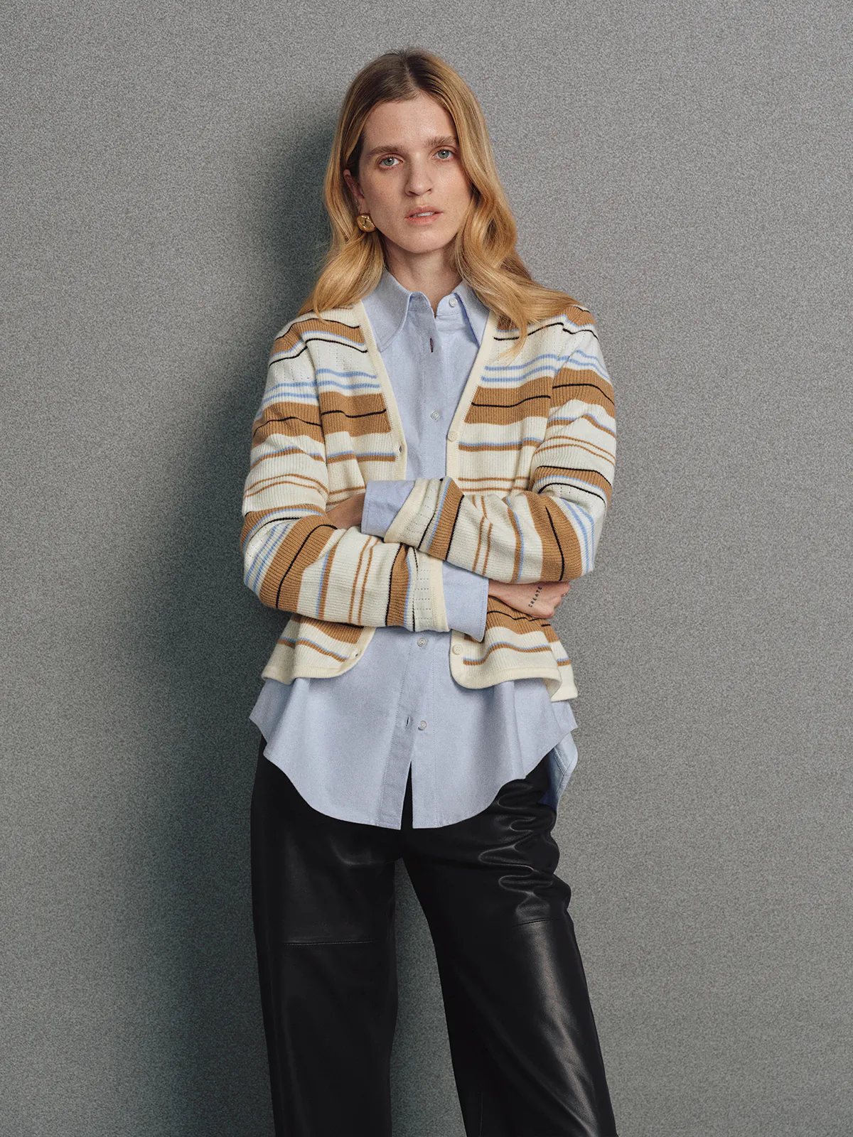 Model in the Camel multicolour stripe V-neck cardigan layered over a turtleneck and trousers, hands in pockets, side view.