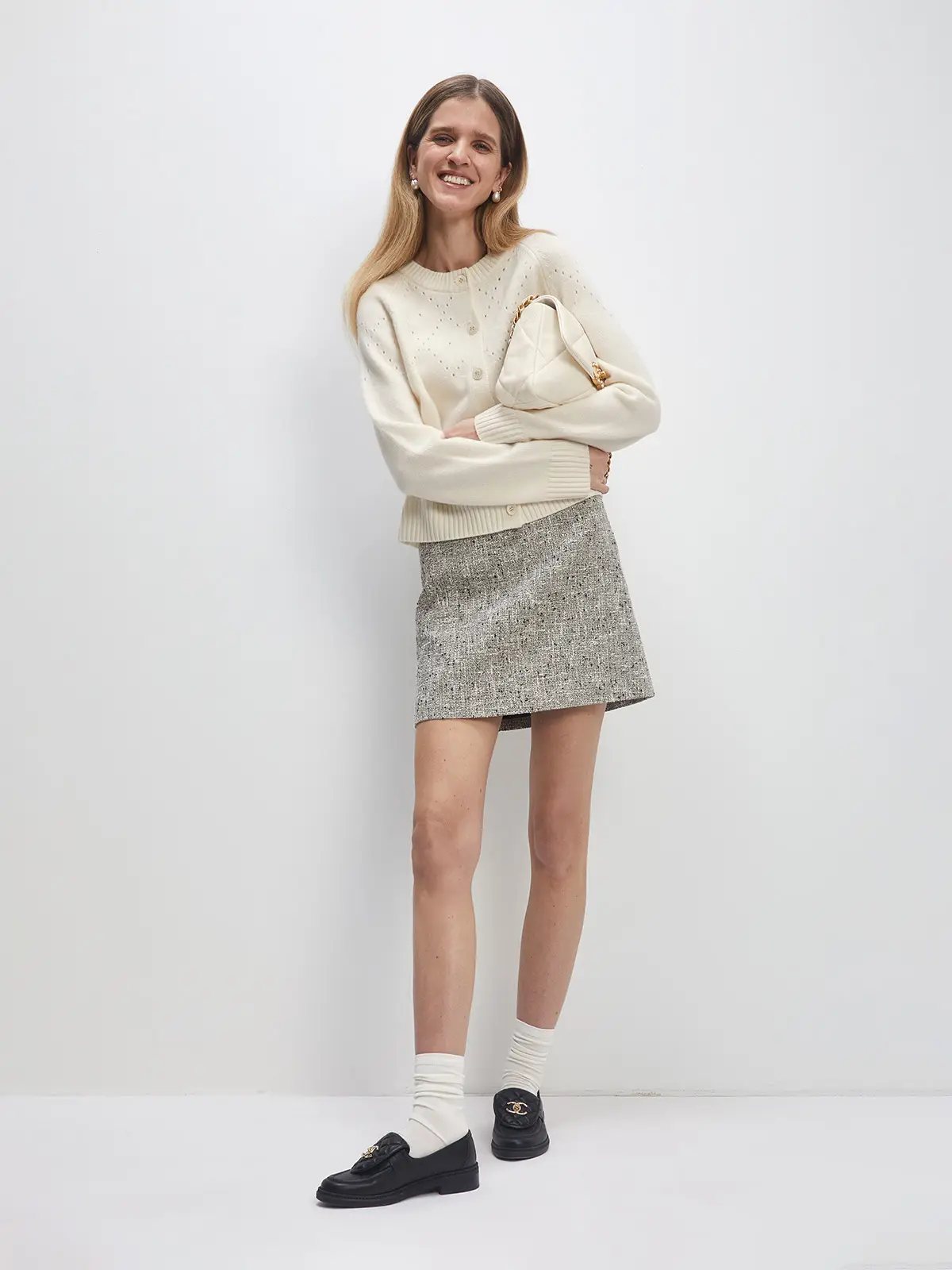 Model wearing a white Fair Isle hollowed knitted cardigan with button front, paired with a tweed mini skirt and loafers.
