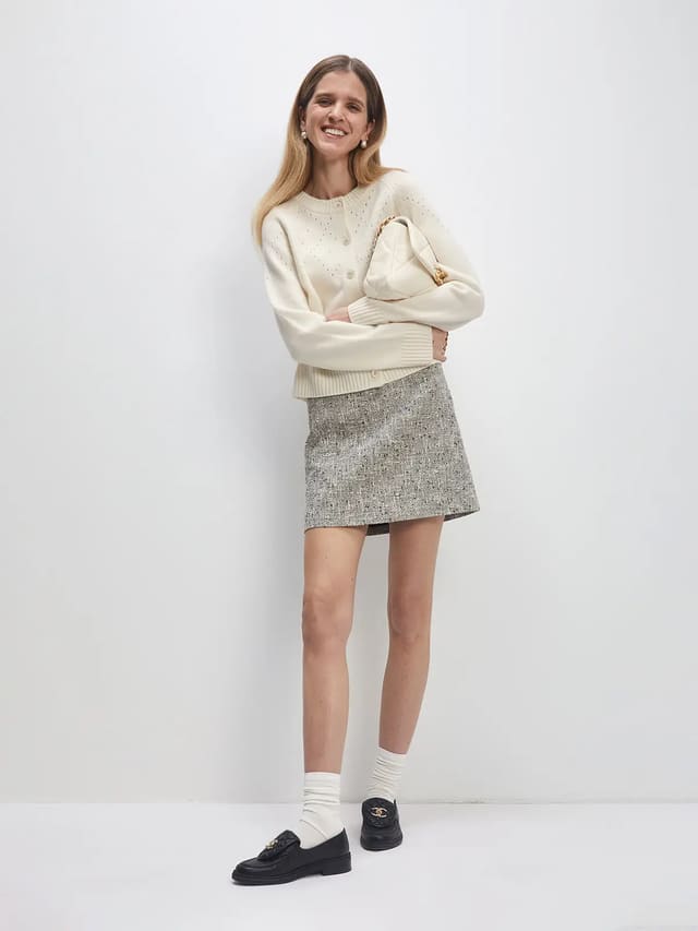 Model wearing a white Fair Isle hollowed knitted cardigan with button front, paired with a tweed mini skirt and loafers.