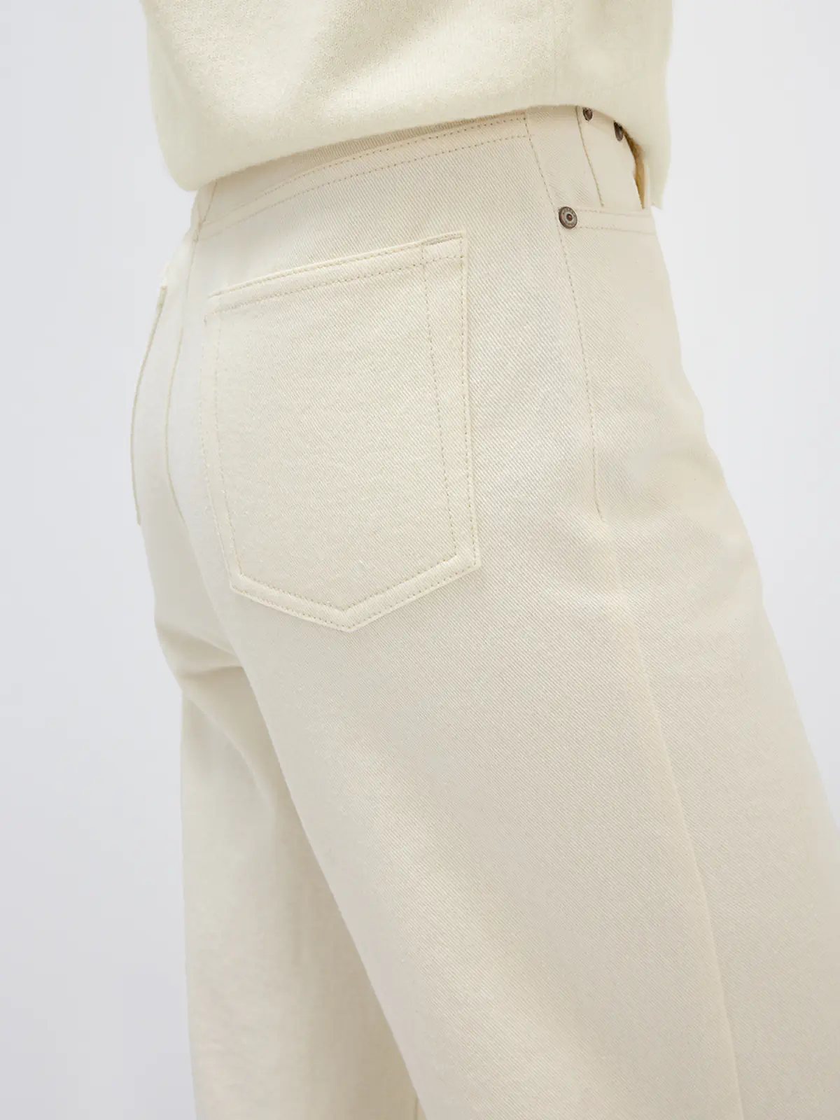 Side view of model in white denim-look curved-leg trousers, patterned cardigan, turtleneck, and loafers.